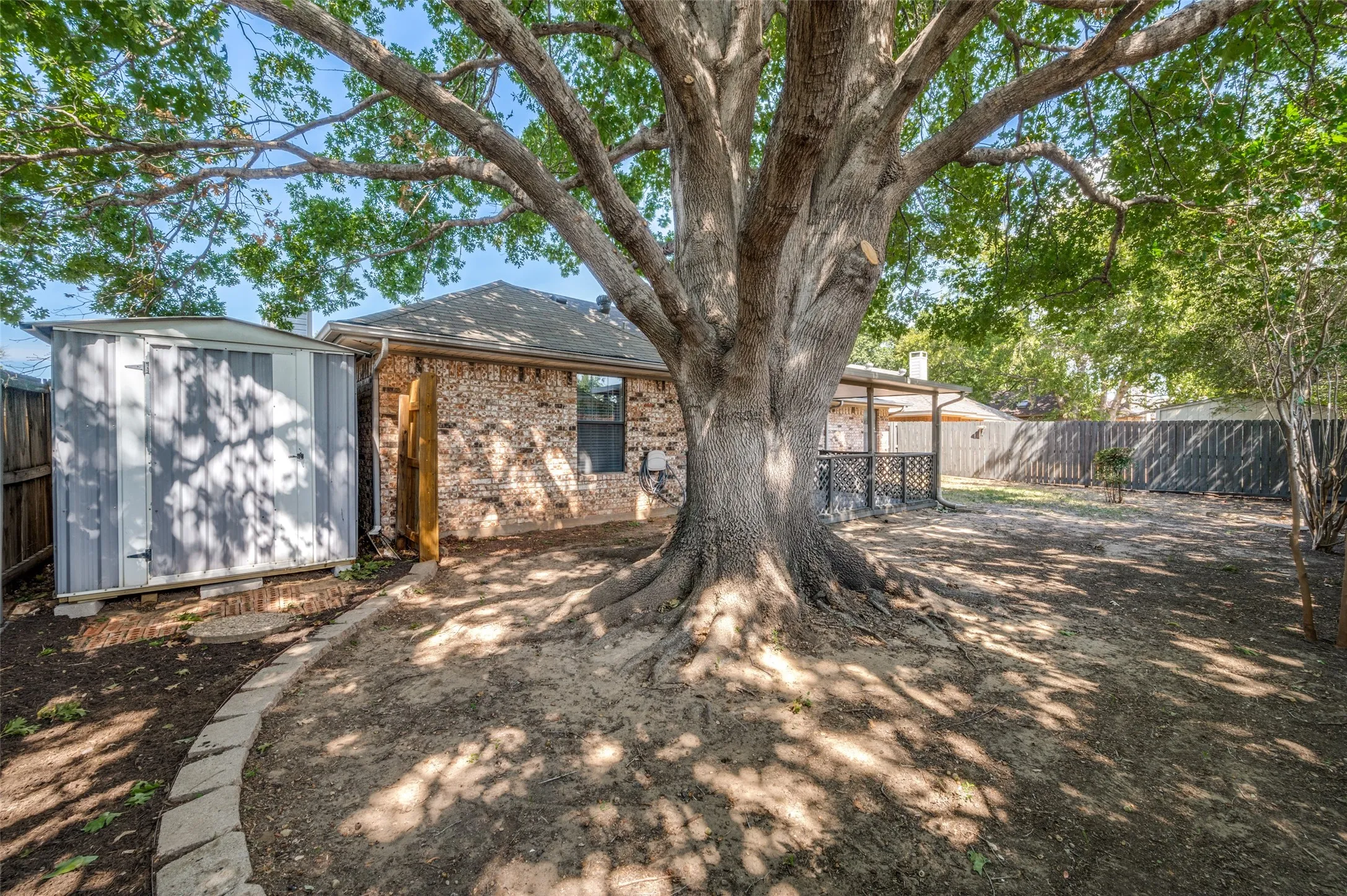 Spacious backyard featuring a substantial mature tree, brick exterior, covered patio, and privacy fencing