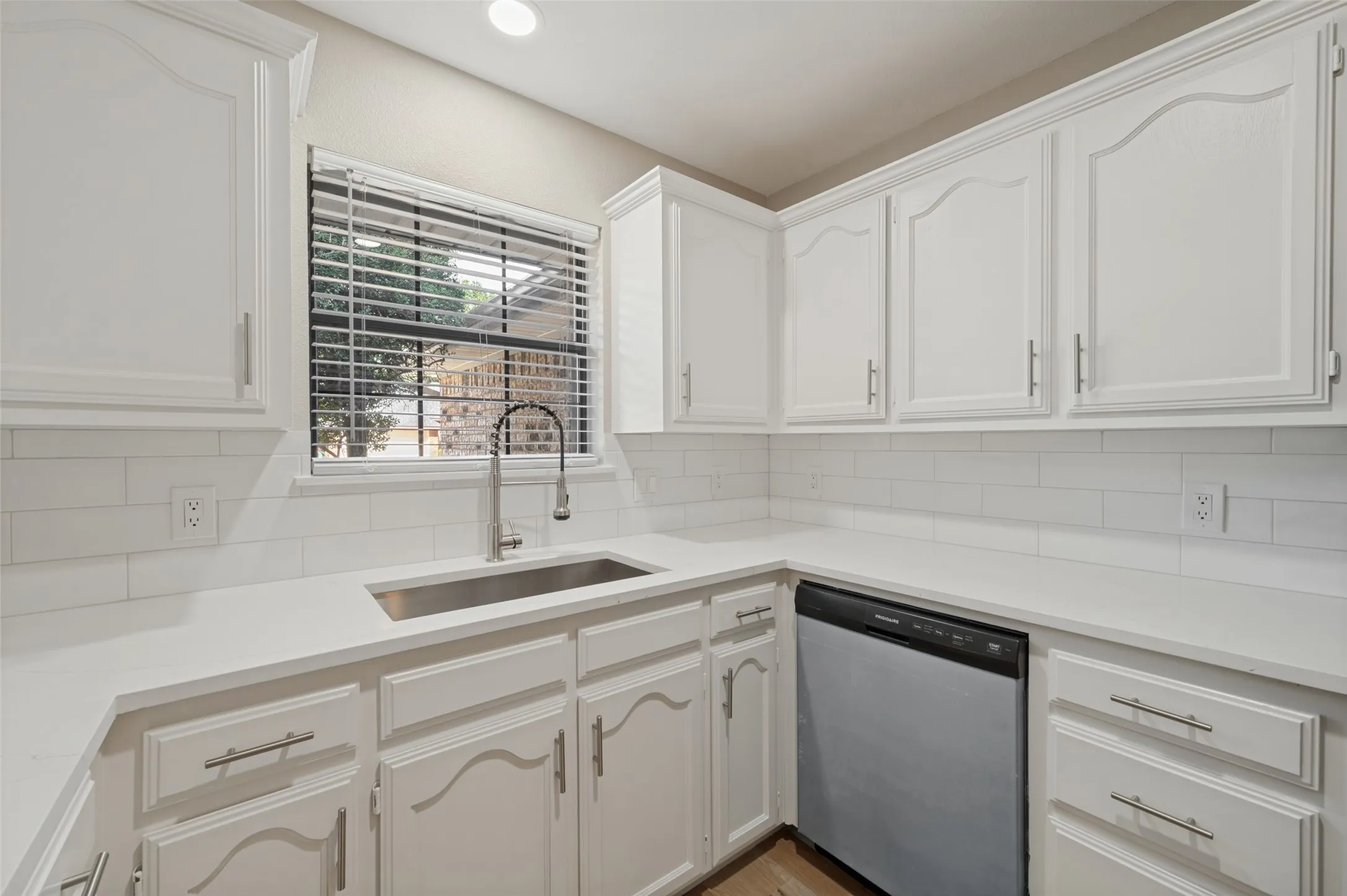 White cabinetry with brushed nickel hardware, quartz countertops, subway tile backsplash, stainless steel undermount sink, and integrated dishwasher