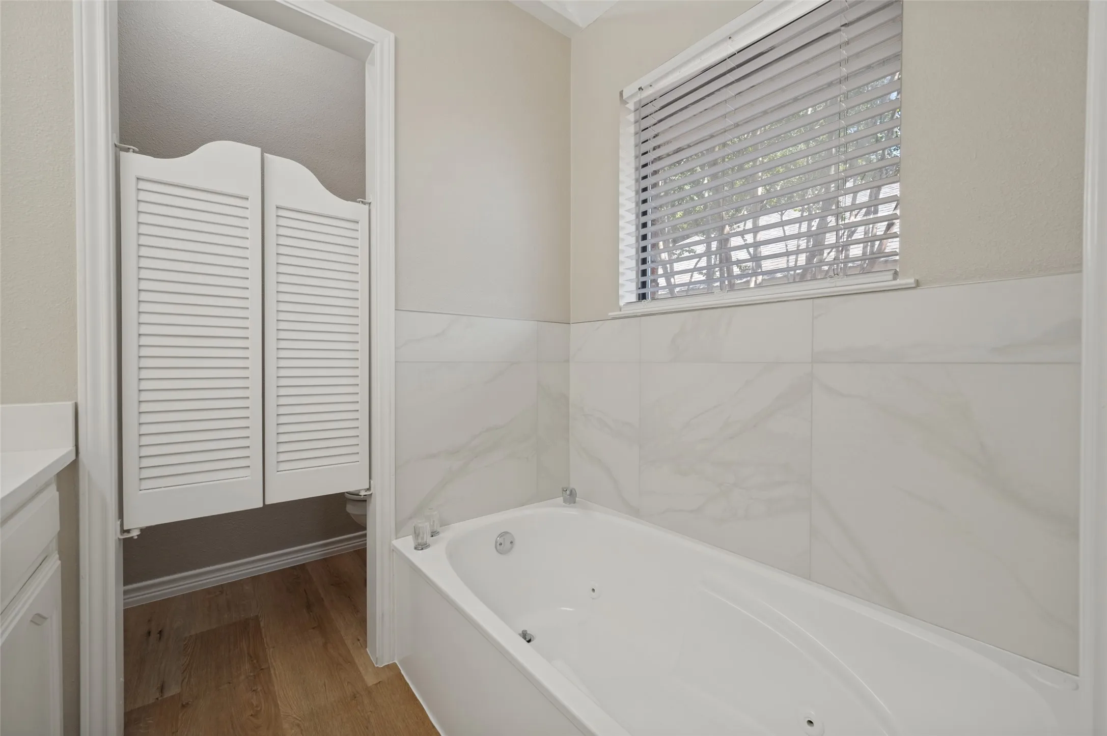 Soaking tub with integrated jets, white tiled bath surround, and a window with horizontal blinds