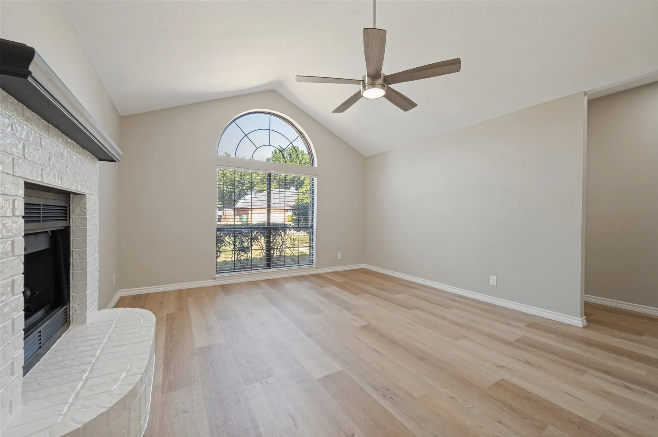 Vaulted ceiling with a contemporary ceiling fan, arched window, fireplace with a white brick surround, and LVP flooring
