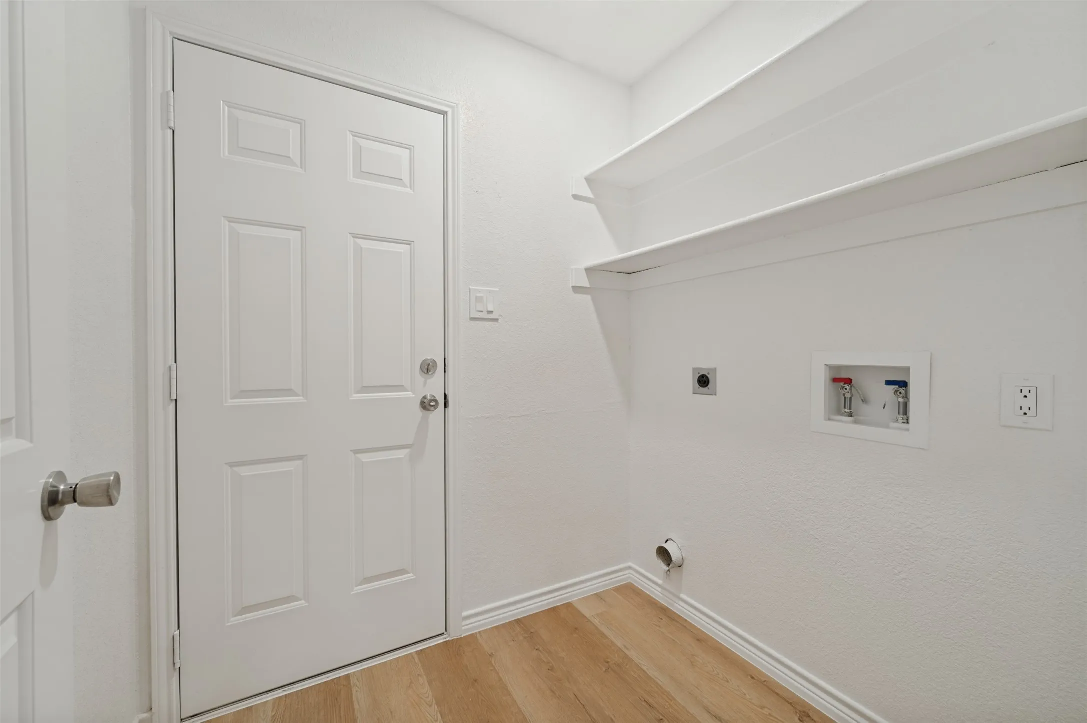 Utility area featuring LVP flooring, built-in shelving, and a panel door with brushed nickel hardware