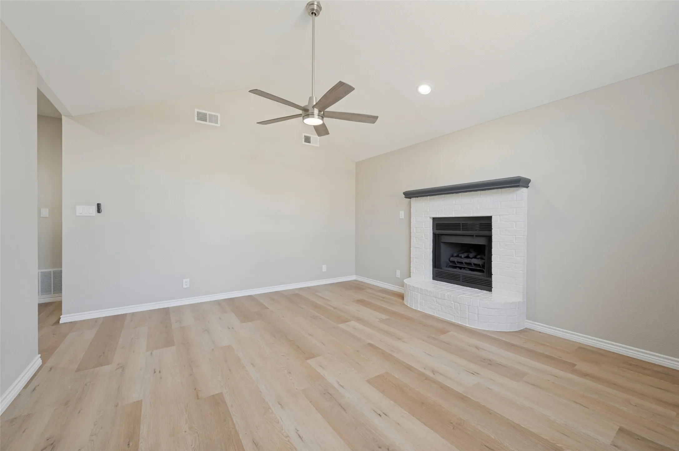 Vaulted ceiling with a contemporary ceiling fan, recessed lighting, LVP flooring, and a white brick fireplace with a dark mantel