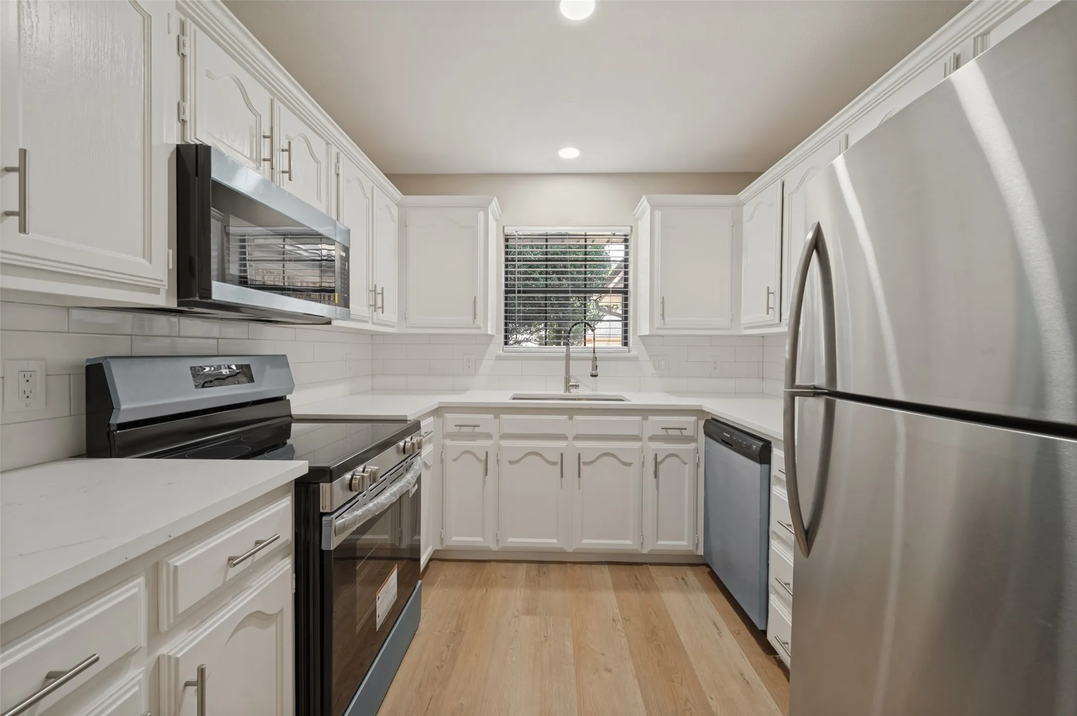 White cabinetry with brushed nickel hardware, stainless steel appliances, white subway tile backsplash, white countertops, and LVP flooring
