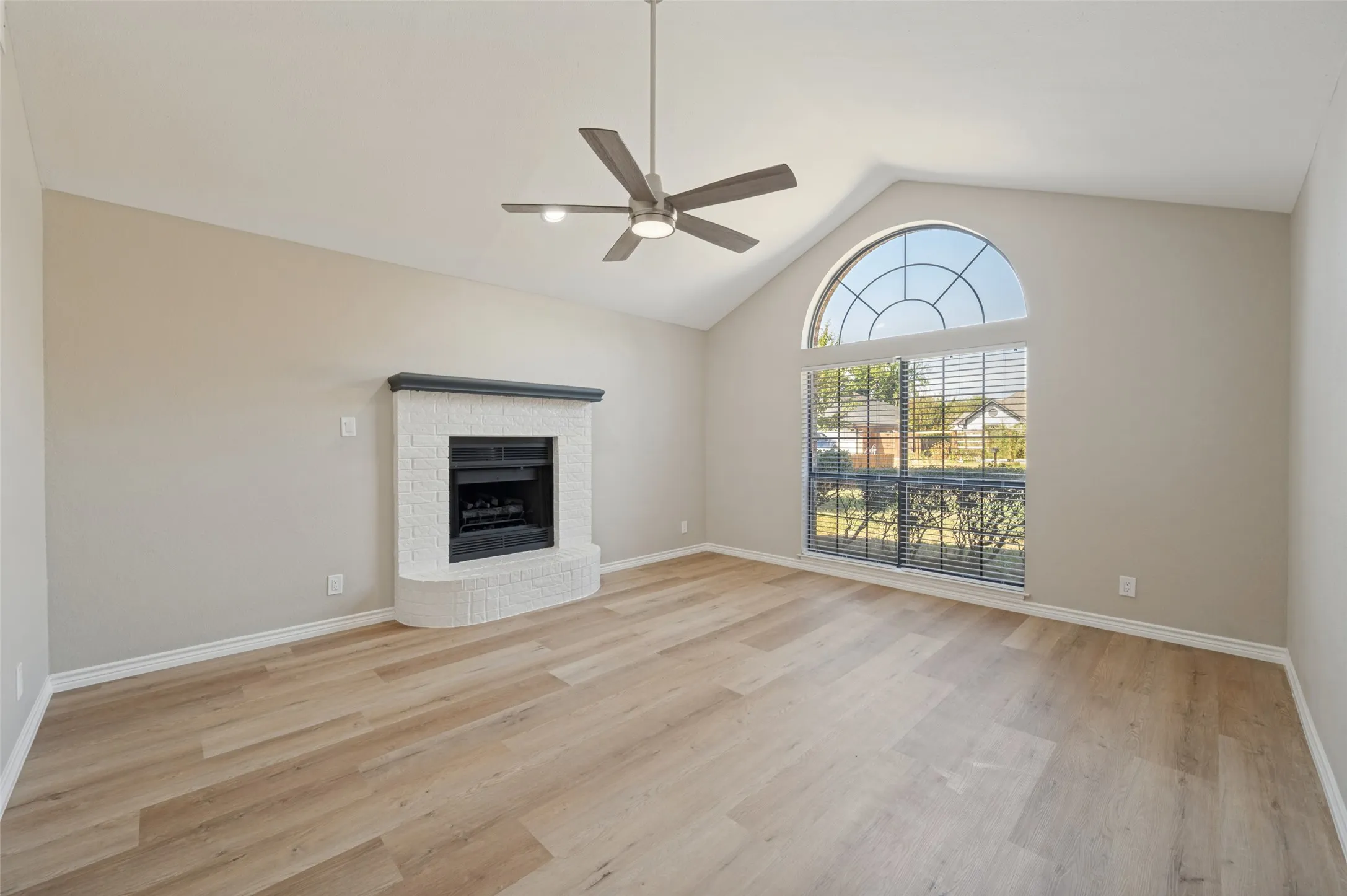 Vaulted ceiling with a ceiling fan, fireplace with a mantle, large arched window, and LVP flooring