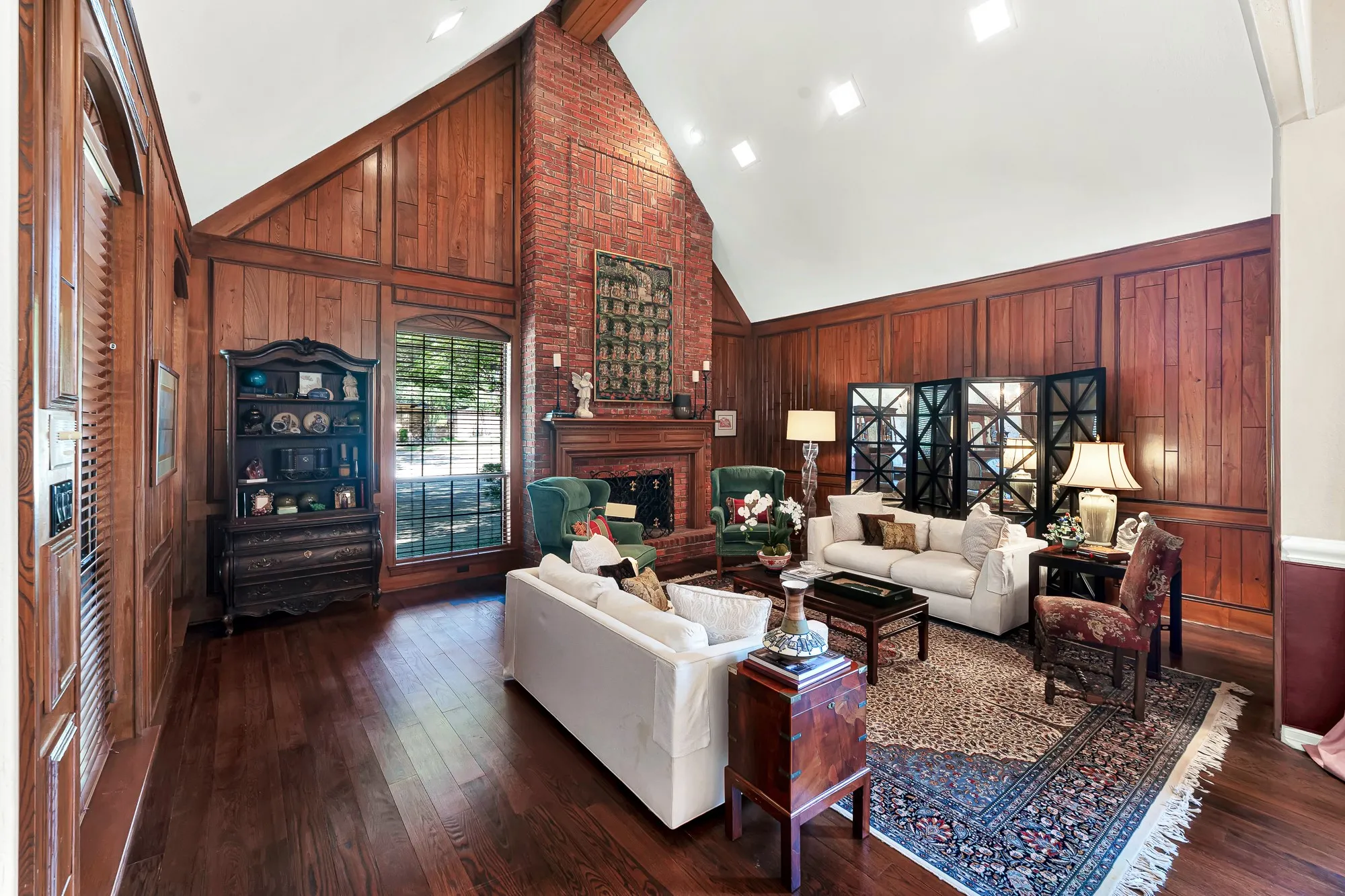 Elegant living room showcasing rich wood-paneled walls, warm hardwood floors, and a striking floor-to-ceiling brick fireplace with custom wood mantel, creating a sophisticated and inviting gathering space.