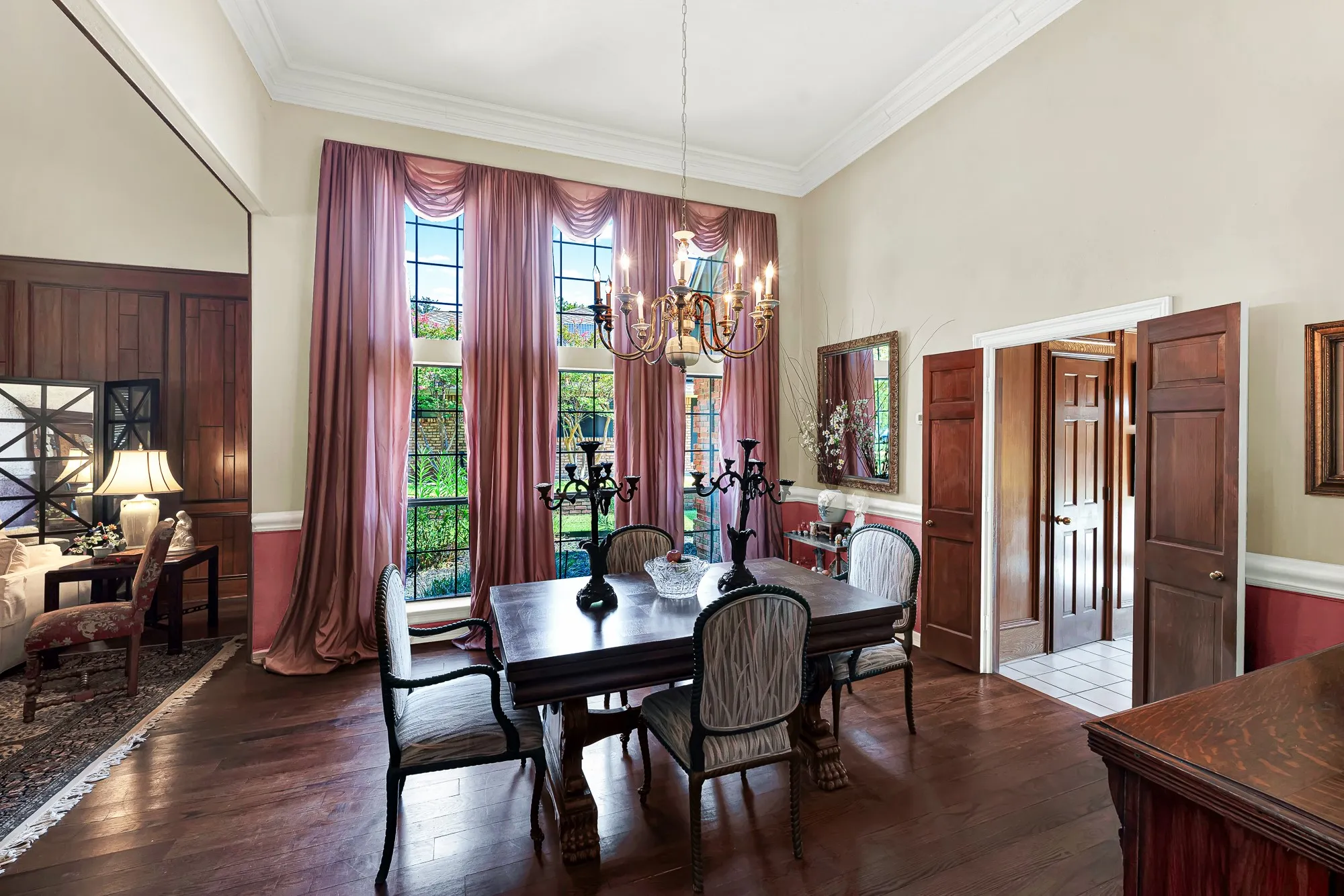 Refined formal dining room with soaring windows, rich hardwood floors, elegant millwork, and a striking statement chandelier.