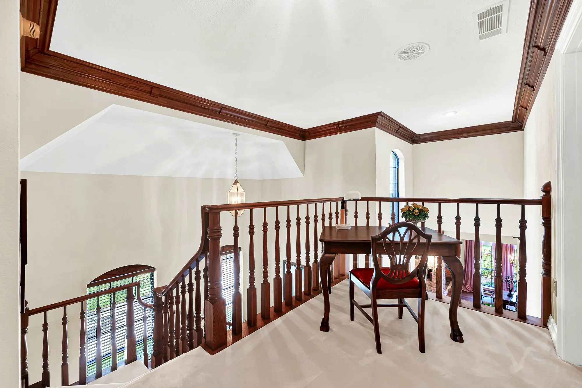 Elegant upstairs landing overlooking the two-story entry, featuring richly detailed wood railing, turned balusters, and distinctive arched windows.
