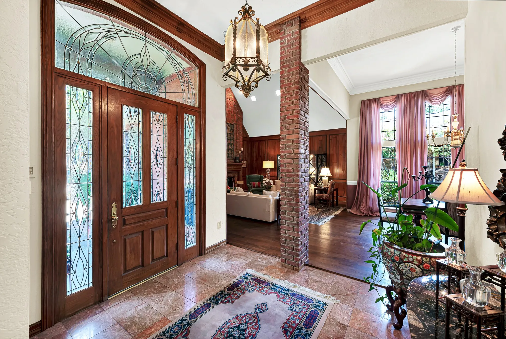 Grand entry foyer featuring a richly crafted wood door with leaded-glass sidelights and transom, rich wood trim, and a distinctive exposed brick column.