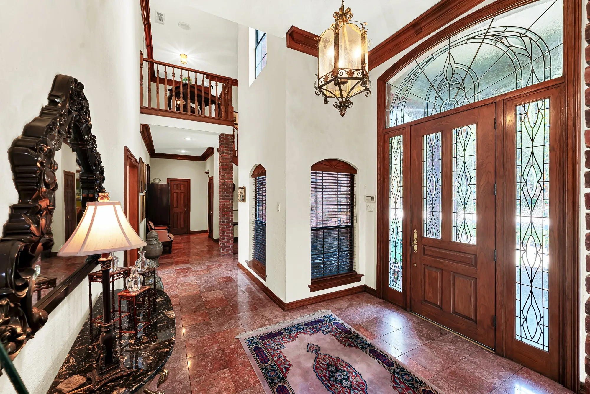 Impressive two-story foyer featuring a beautifully crafted wood entry door with intricate leaded-glass detailing, soaring ceilings, rich wood accents, and an elegant lantern-style chandelier.