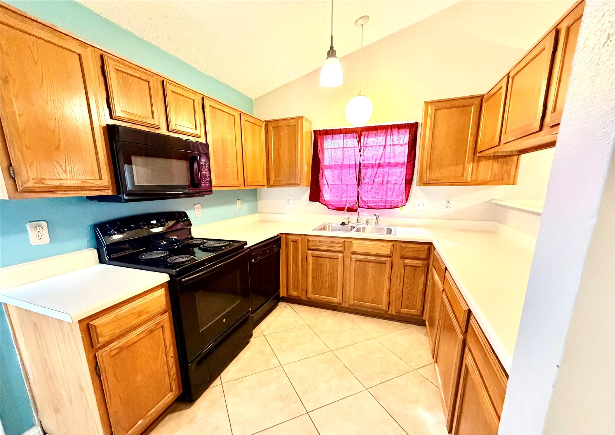 U-shaped kitchen featuring wood cabinetry, light-toned countertops, black appliances, and a tiled floor