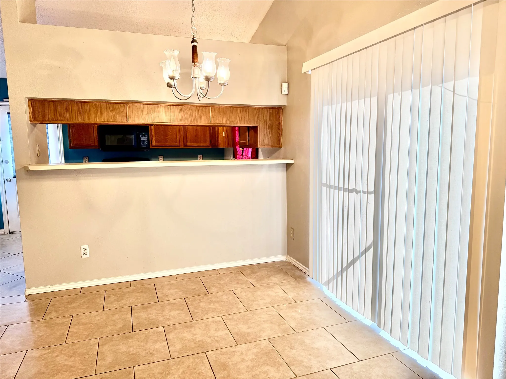 Tile flooring, a built-in breakfast bar with wood-finish cabinetry, vaulted ceiling, and sliding glass door with vertical blinds