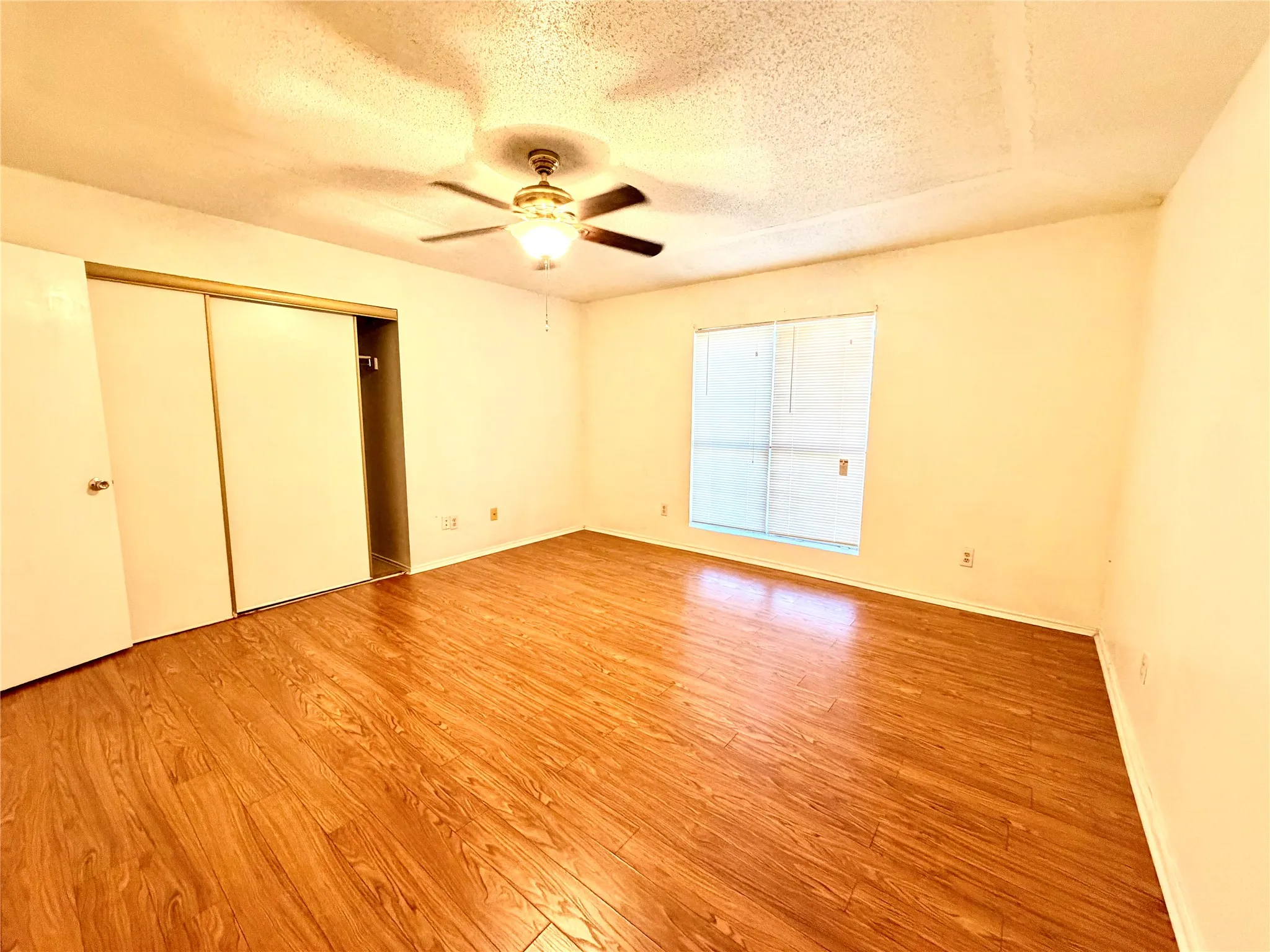 Wood-finish flooring, ceiling fan with integrated lighting, window with blinds, and sliding closet doors