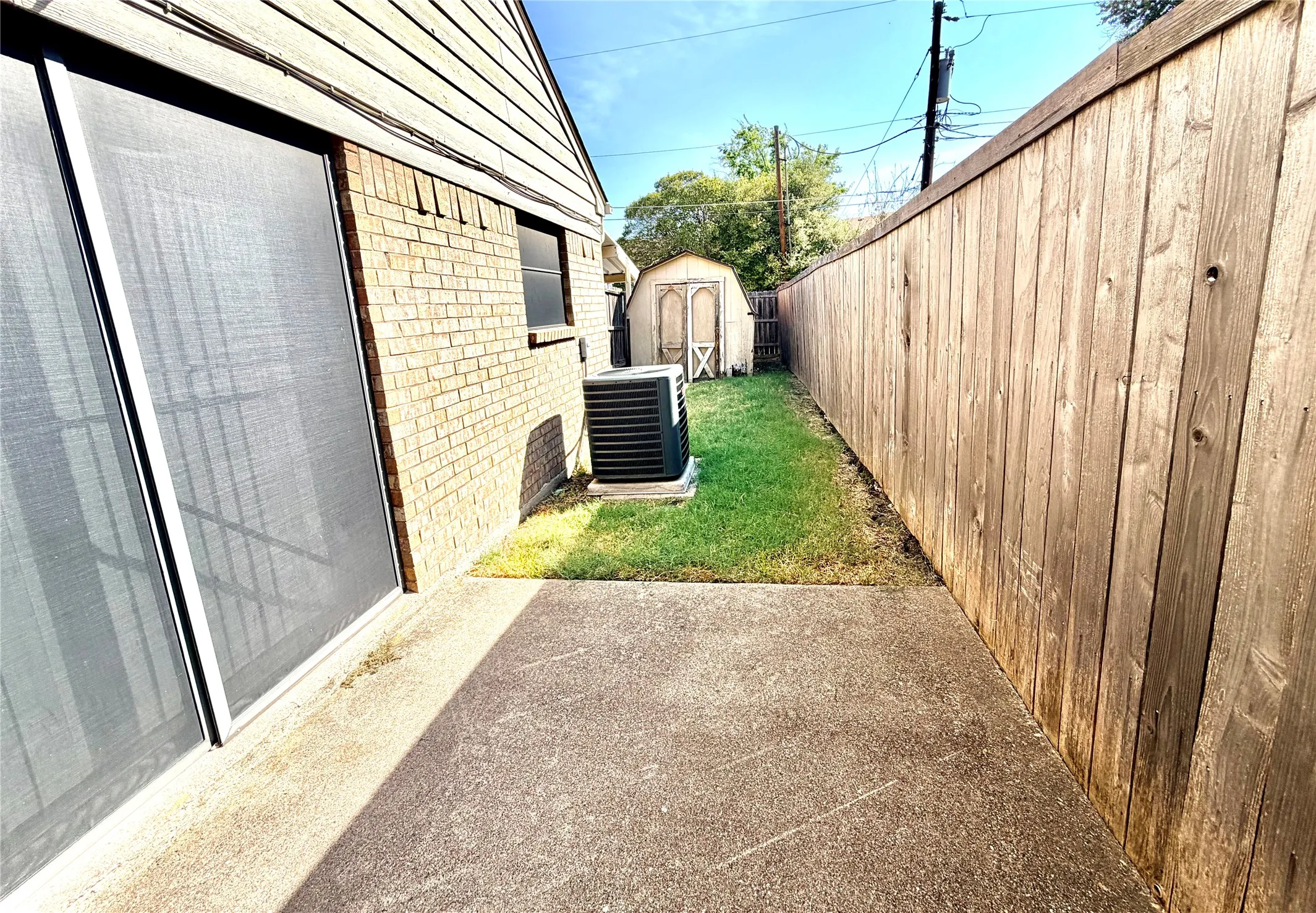 Brick and siding exterior with a sliding glass door, accompanied by a dedicated air conditioning unit and a wooden privacy fence