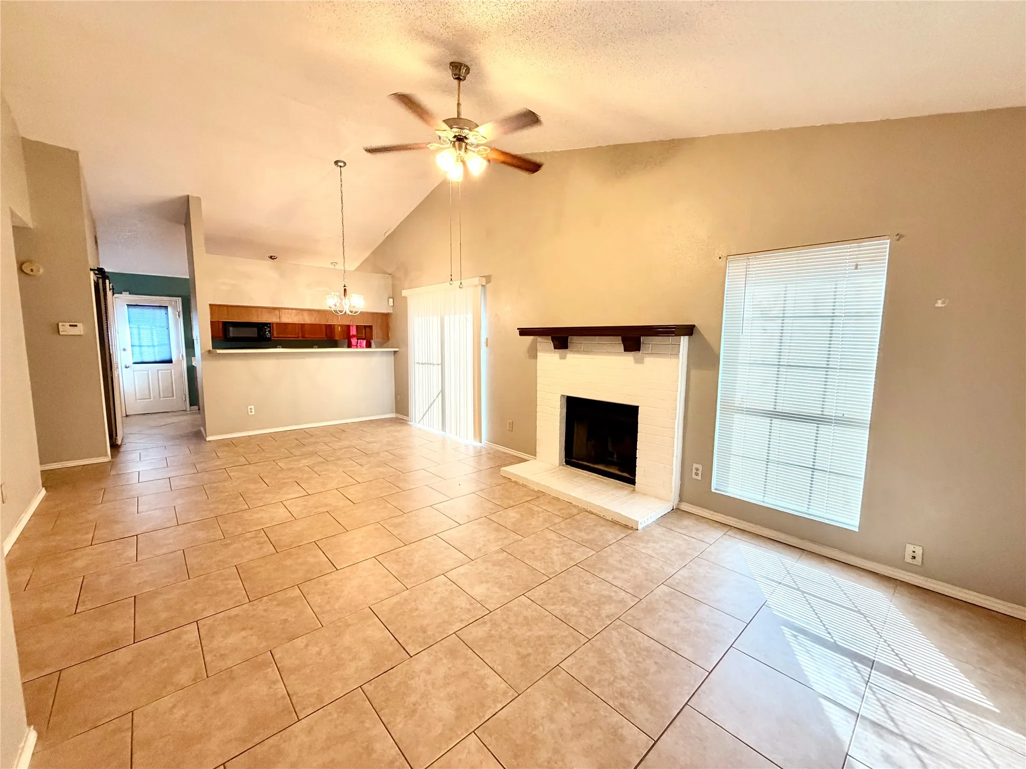 Vaulted ceiling with ceiling fan, tile flooring, brick fireplace with wood mantel, and sliding glass door