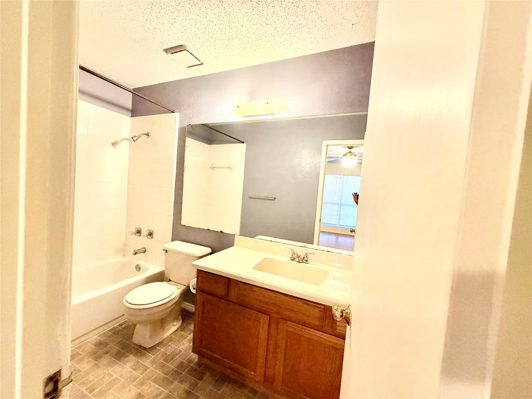 Tub/shower combination with chrome fixtures, single vanity with wood-finish cabinetry, and a large wall-mounted mirror
