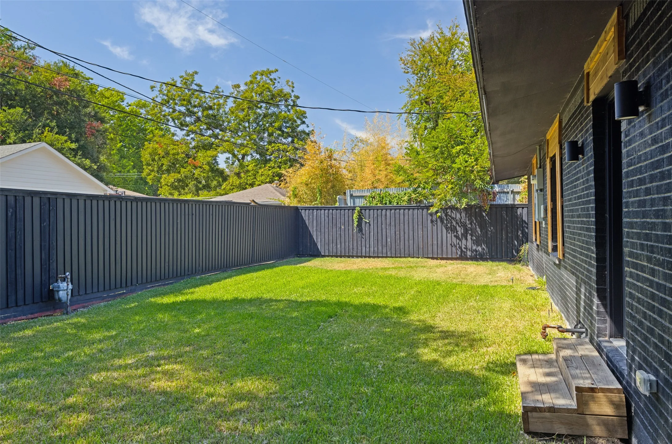 Expansive grass yard with a dark privacy fence and a dark brick exterior