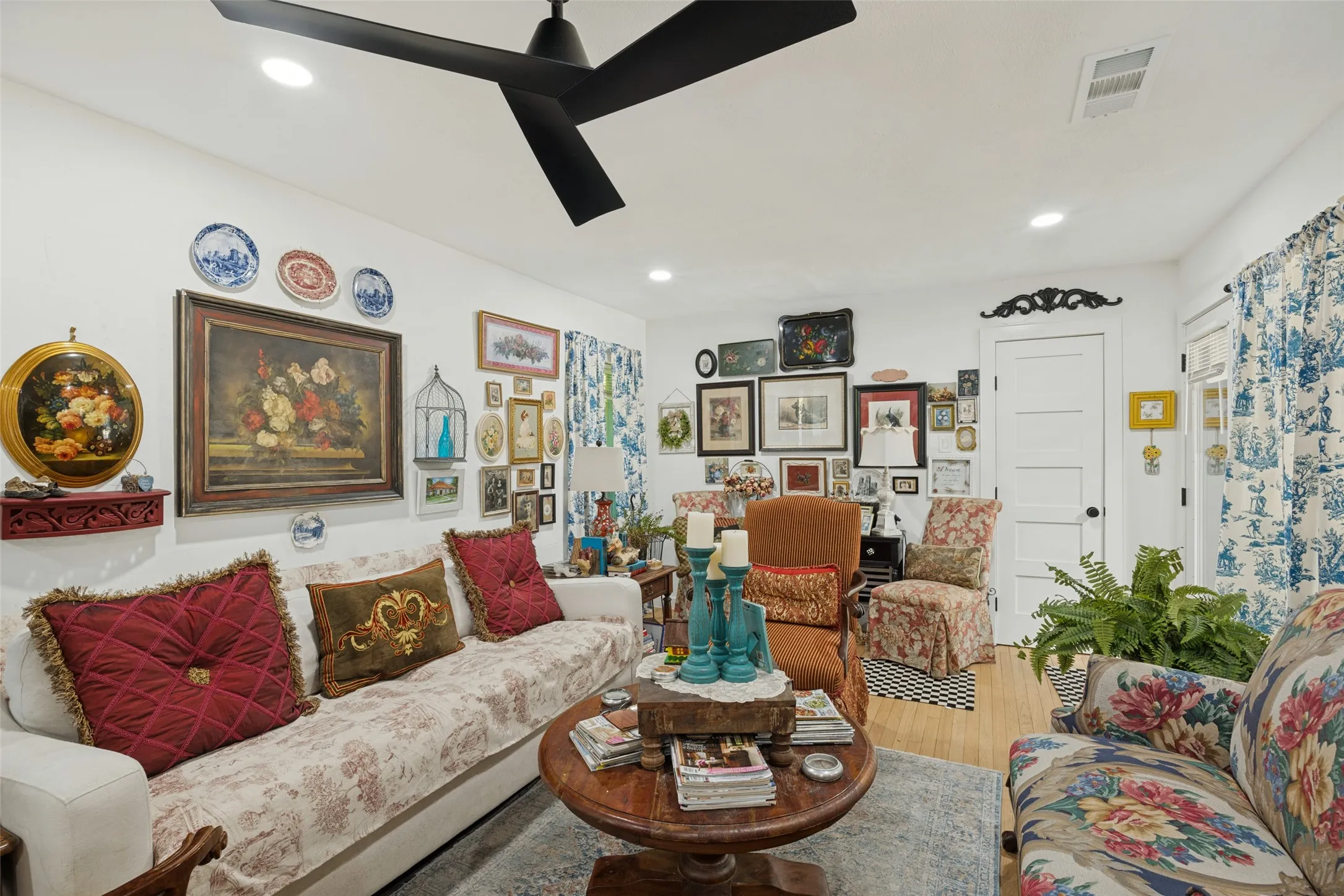 Recessed ceiling lighting, a modern black ceiling fan, white paneled door, and wood-finish flooring