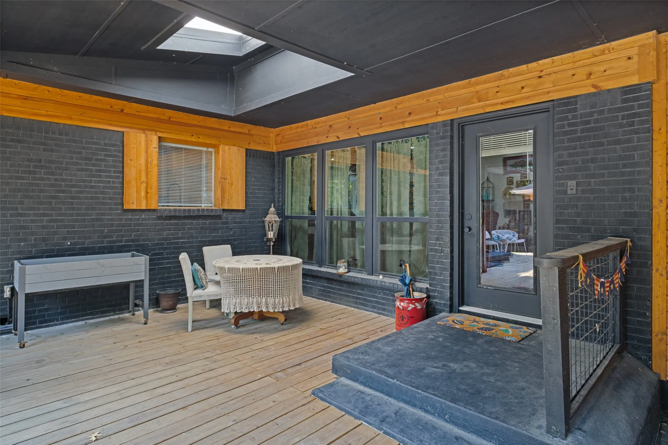 Covered patio featuring wood-finish flooring, dark brick walls, and a skylight