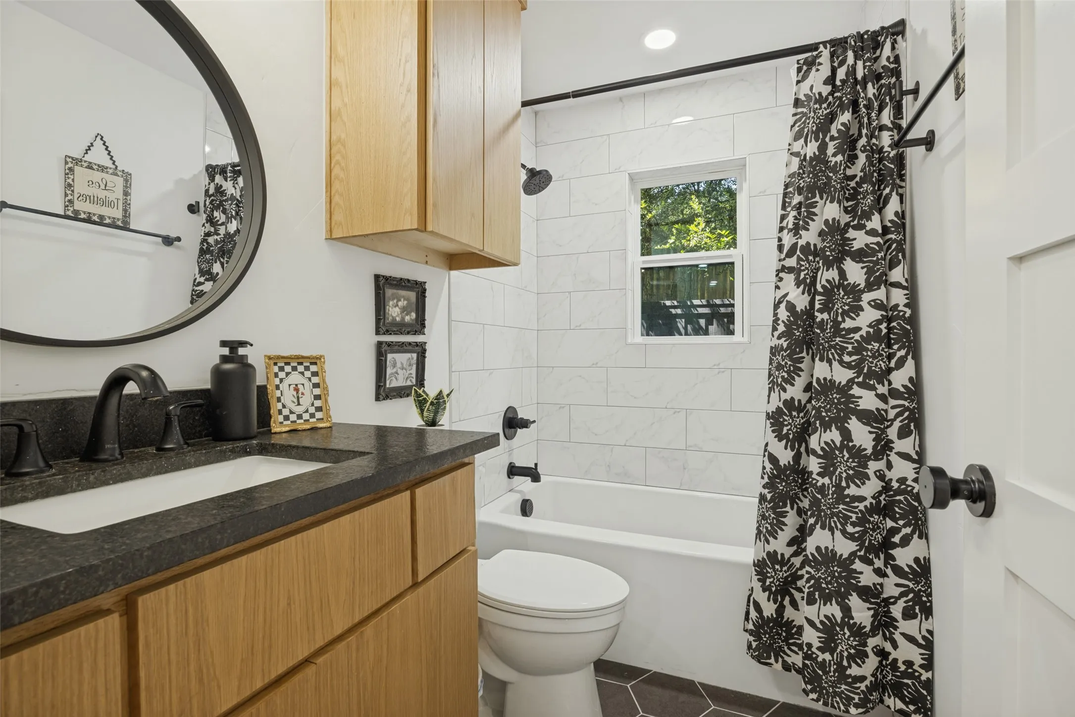 Bathroom featuring a wood-finish vanity with an undermount sink, dark countertop, matte black fixtures, and a tiled shower-bath combination