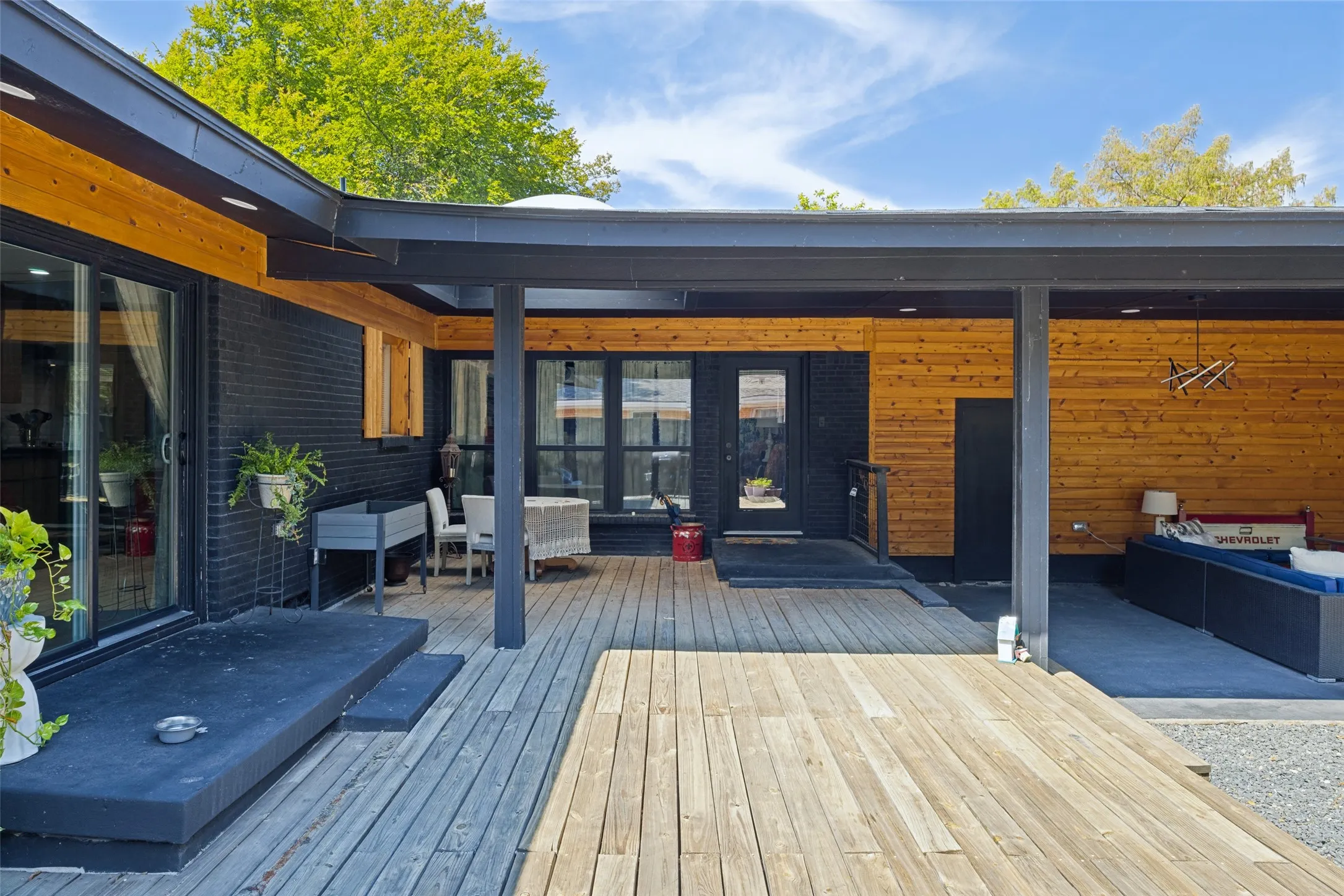 Expansive outdoor deck with natural wood planks, a covered patio area, and exterior walls featuring both dark brick and natural wood siding