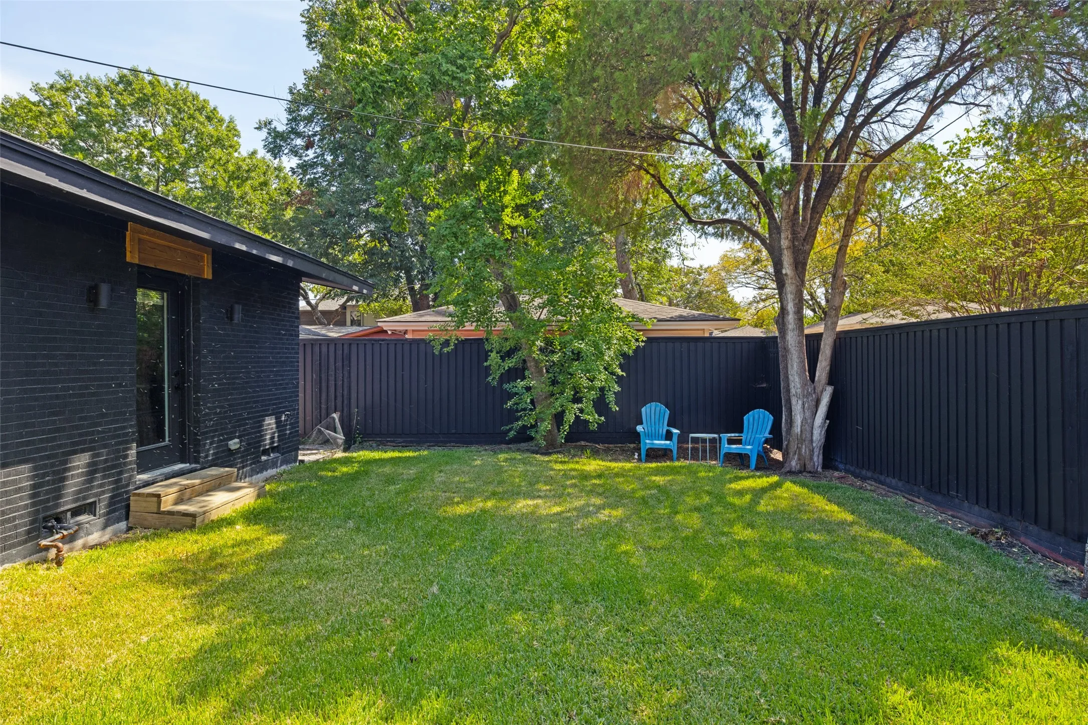 Expansive lawn area, dark painted brick exterior, privacy fencing, mature trees, and a glass-paneled exterior door