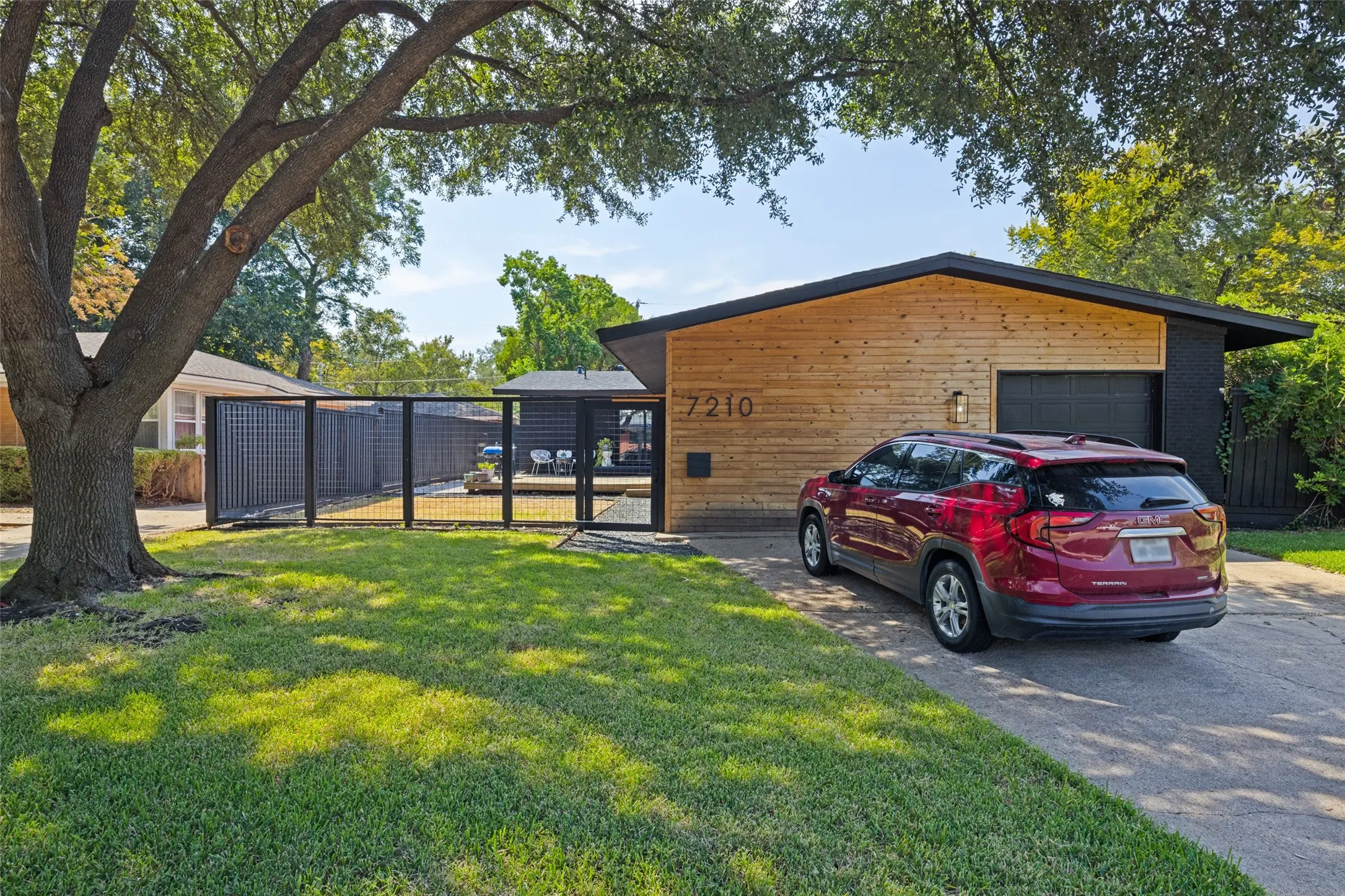 Sloped roofline residence featuring horizontal wood siding, an integrated garage with a dark door, and a black metal fence