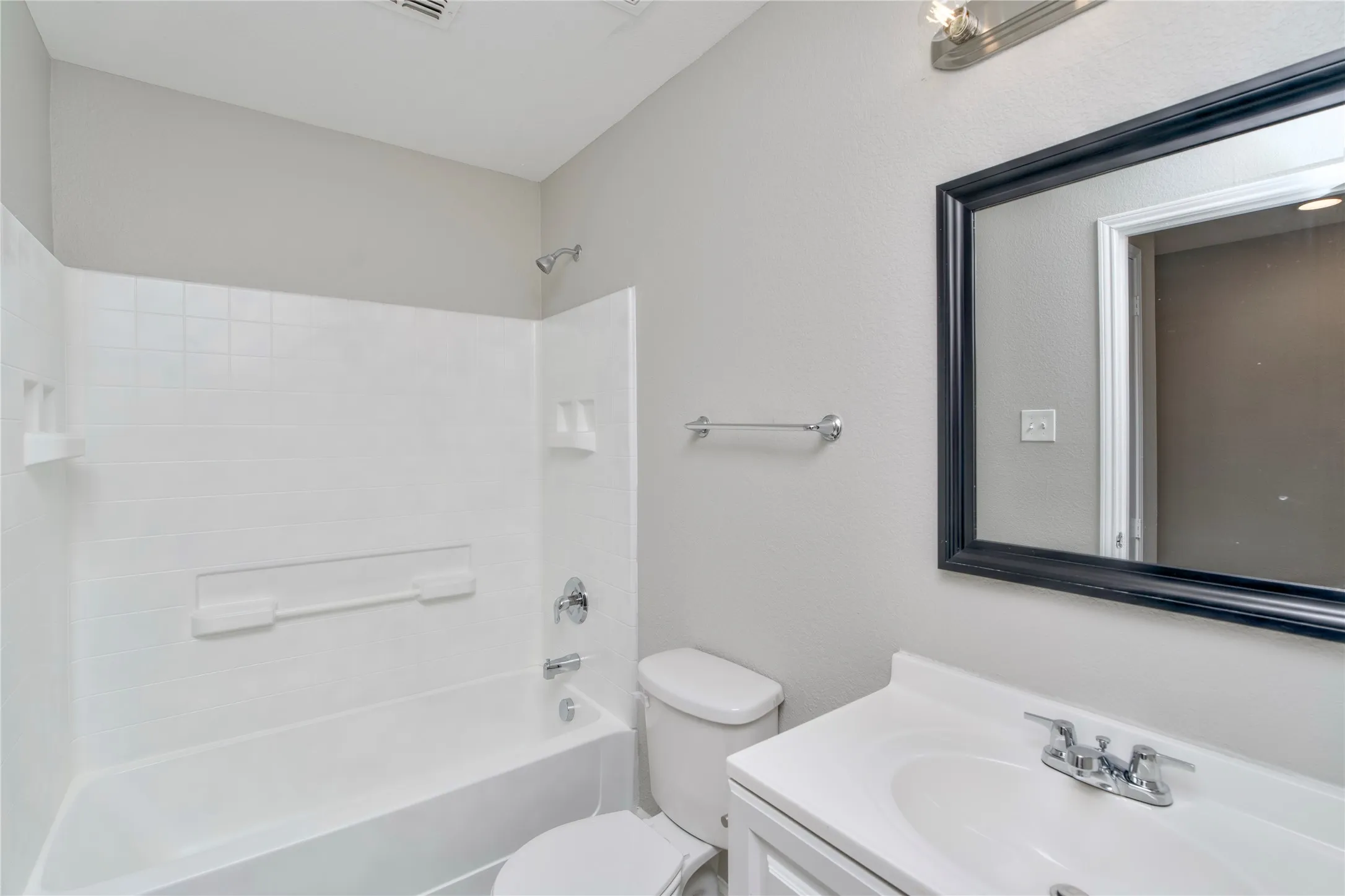 Bathroom with white tile shower surround, chrome fixtures, a white vanity, a framed mirror, and a chrome towel bar