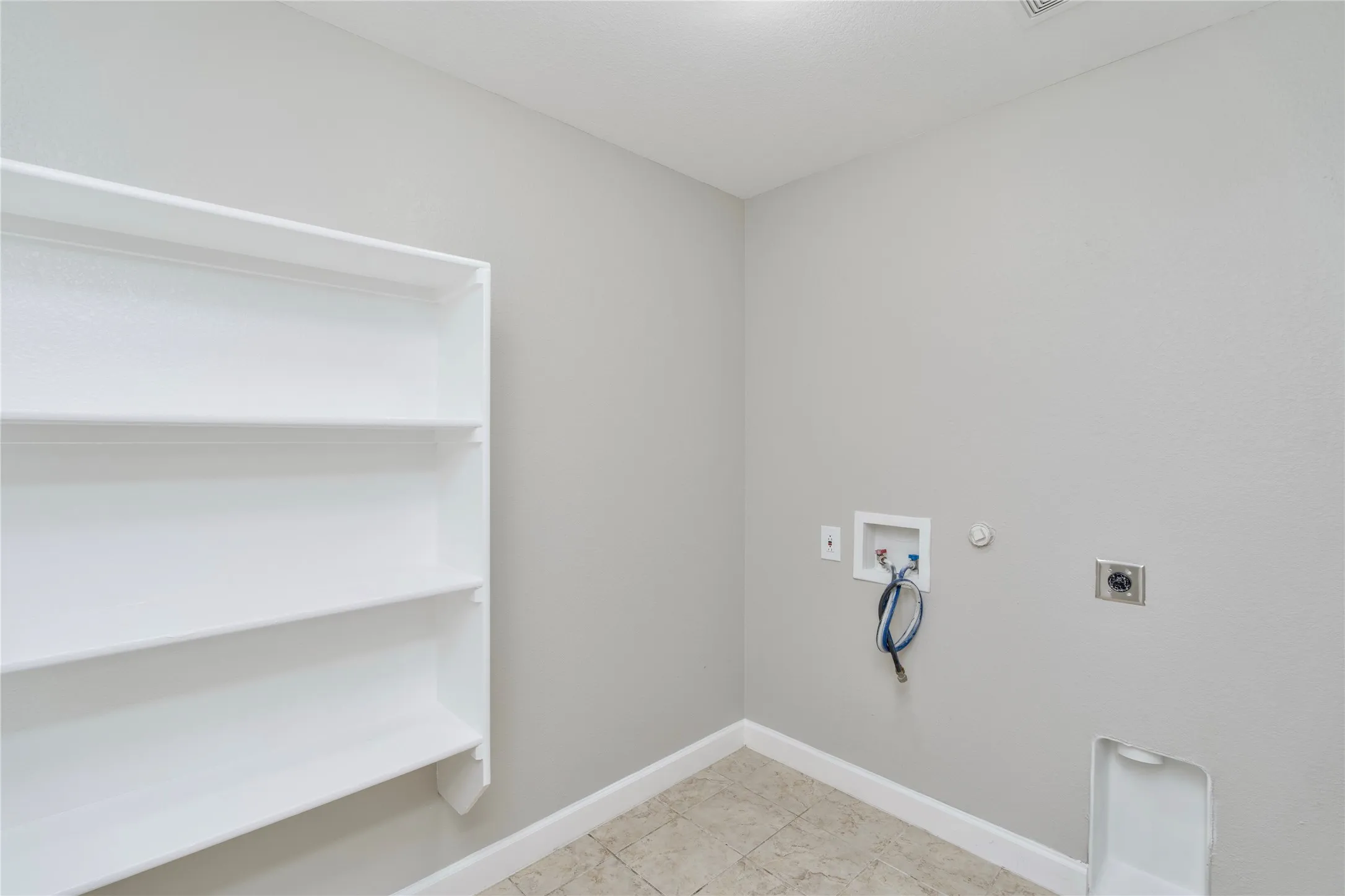 Laundry space featuring a tile floor, light gray walls, white built-in shelving, and utility hookups