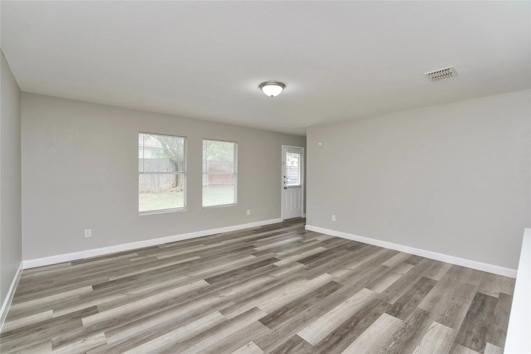 Spacious room featuring wood-finish flooring, light gray walls, multiple windows, and a white paneled door