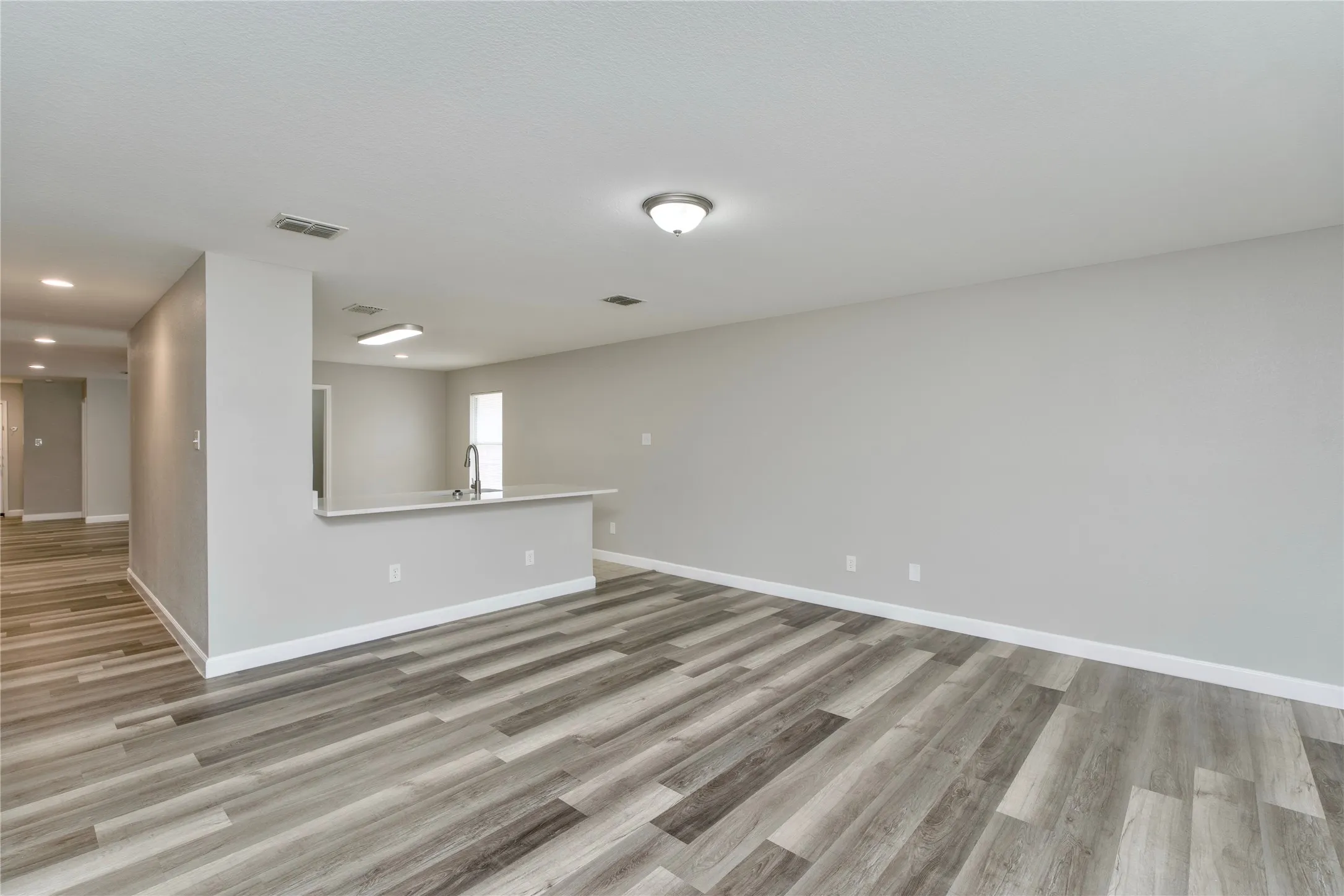 Spacious interior featuring wood-finish flooring, a kitchen peninsula with a sink, and recessed lighting