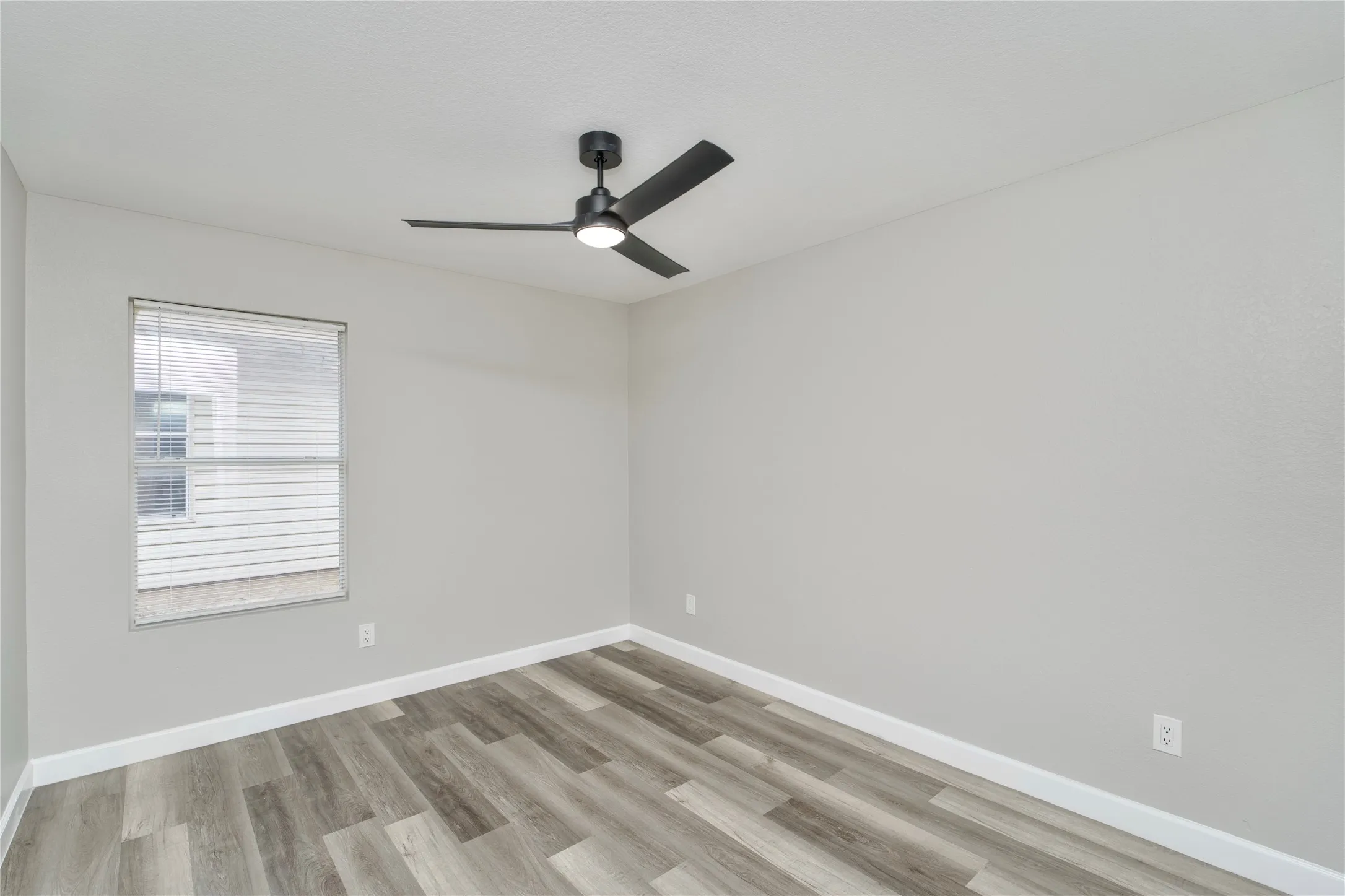 Wood-finish flooring, single window with blinds, ceiling fan with integrated lighting, and light gray wall finish
