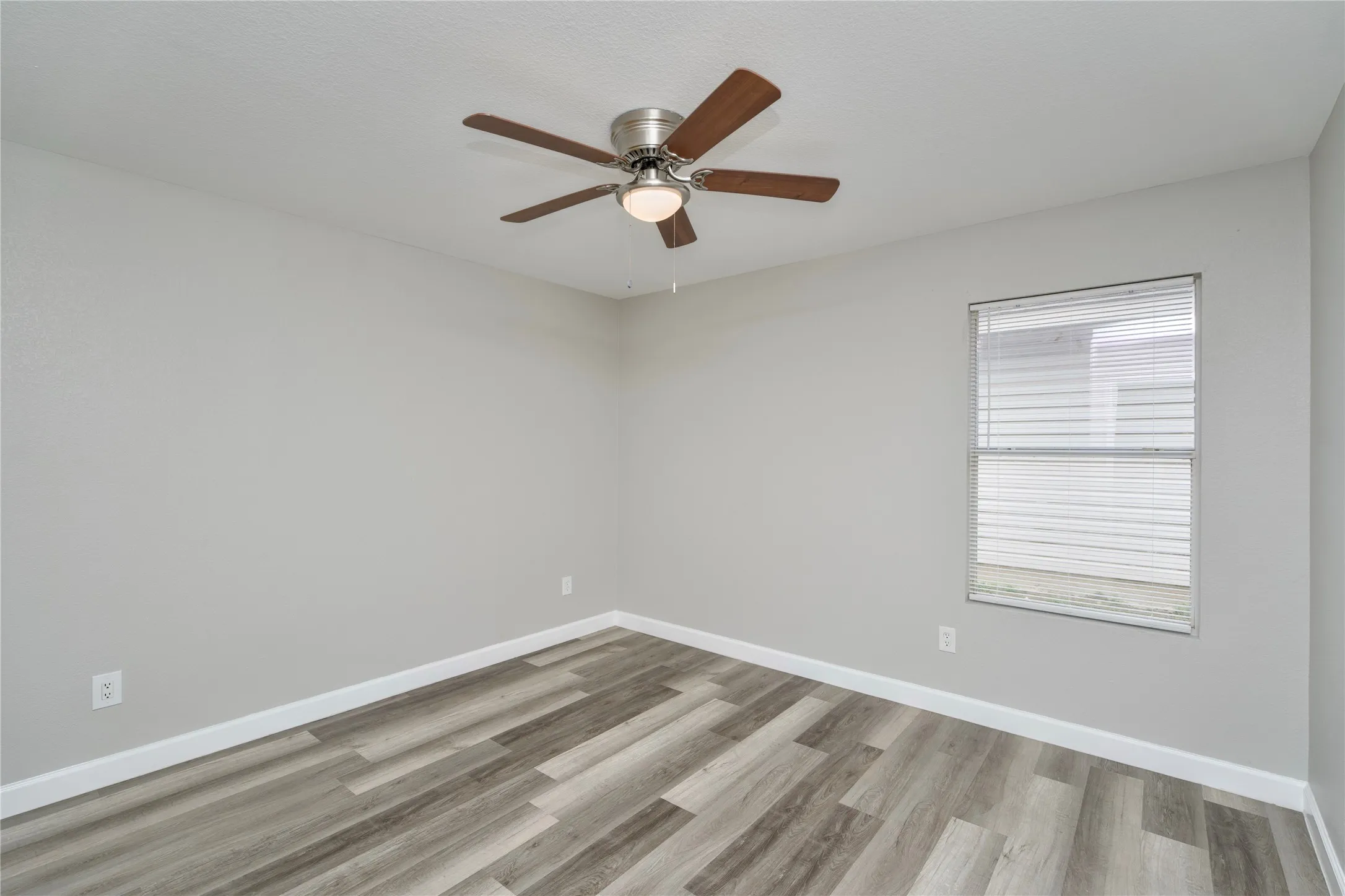 Room with wood-finish flooring, light gray walls, a ceiling fan with integrated lighting, and a window with horizontal blinds