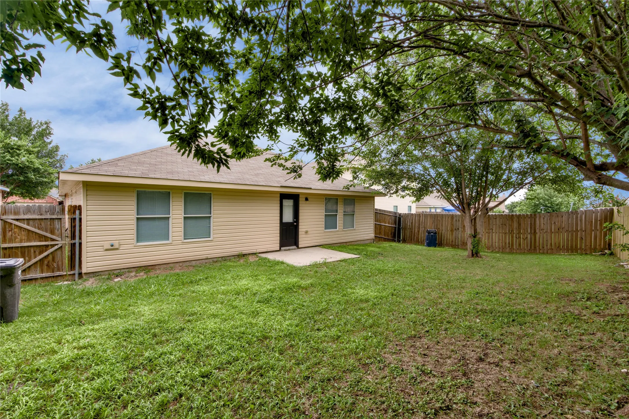 Expansive backyard featuring a manicured lawn, established trees, and a wooden privacy fence
