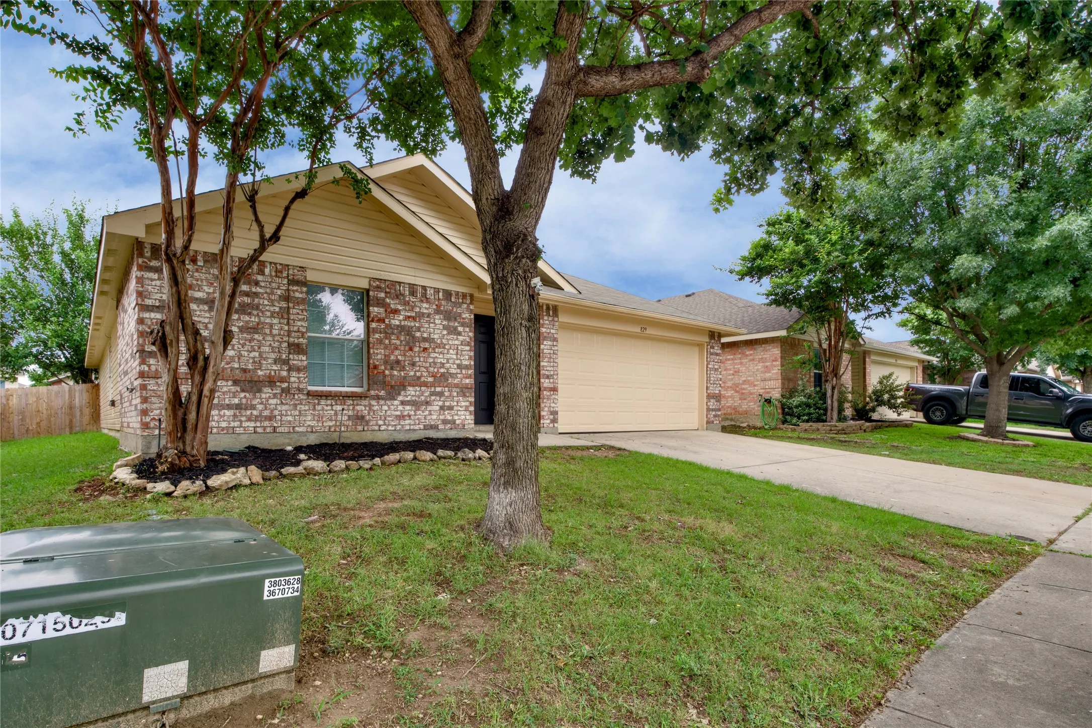 Brick exterior with horizontal siding accents, attached garage, concrete driveway, and mature landscaping