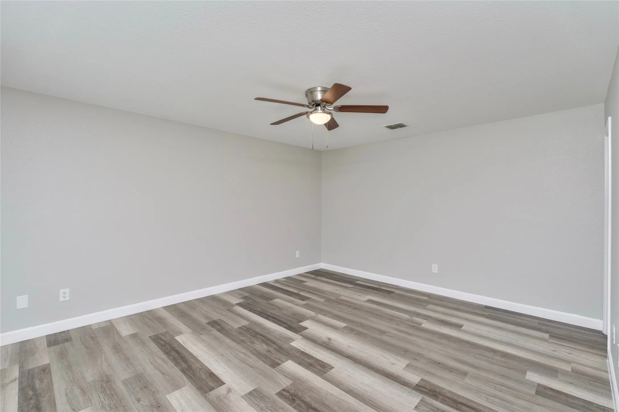 Wood-finish flooring with a varied plank design, neutral wall color, and a ceiling fan with light fixture