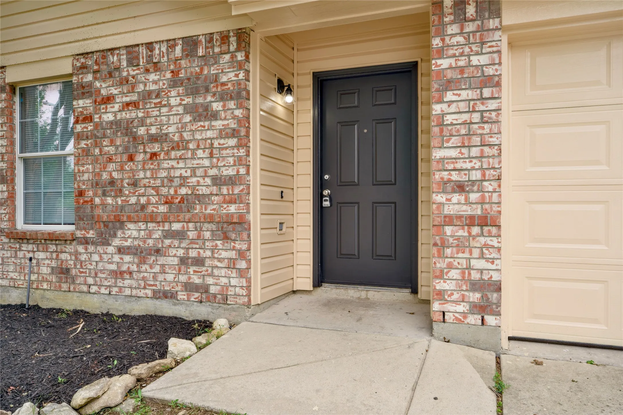 Brick and siding exterior with a paneled front entry door, a window with muntins, and an attached garage door