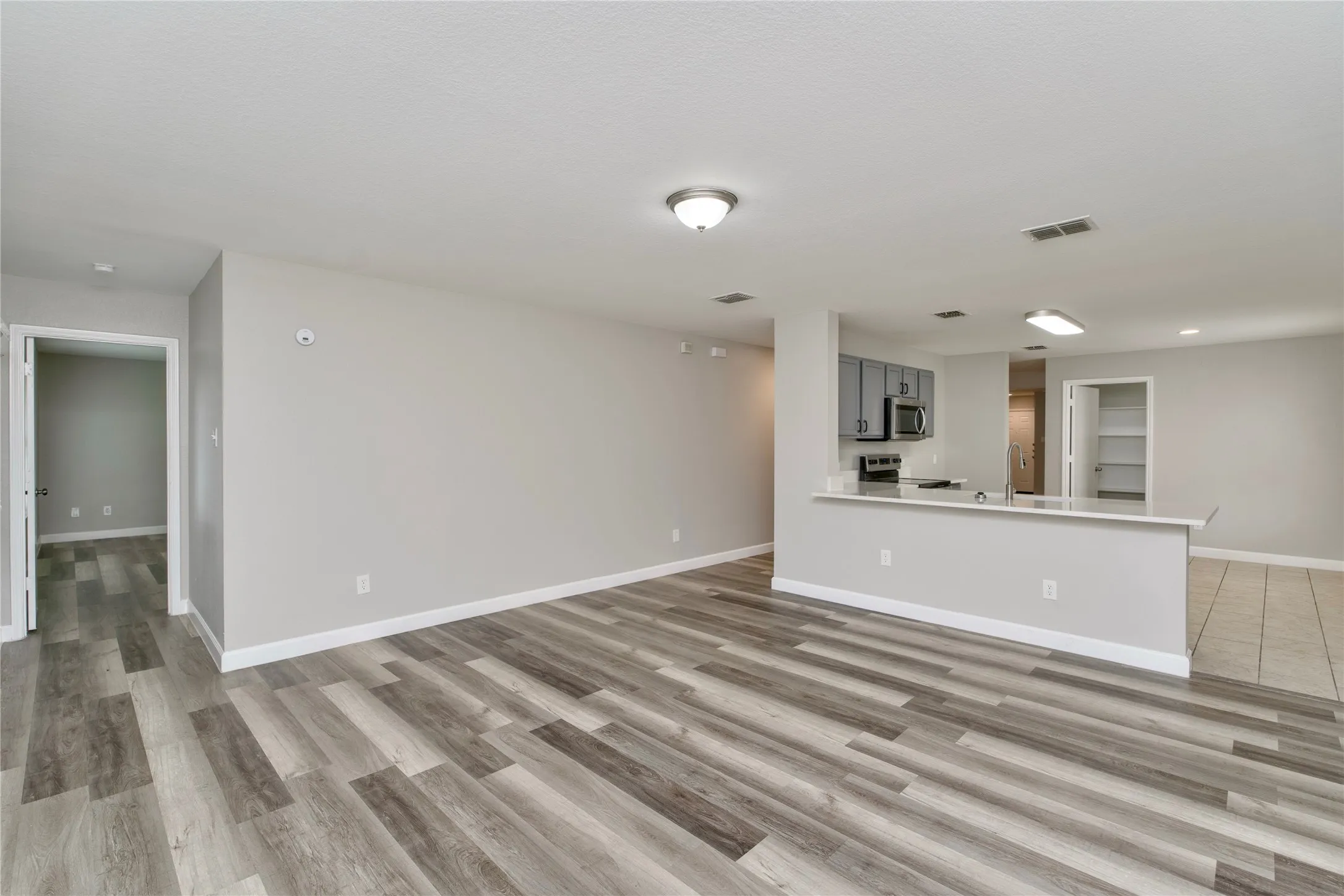 Wood-finish flooring, light gray wall tones, recessed lighting, kitchen peninsula with counter seating, stainless steel appliances