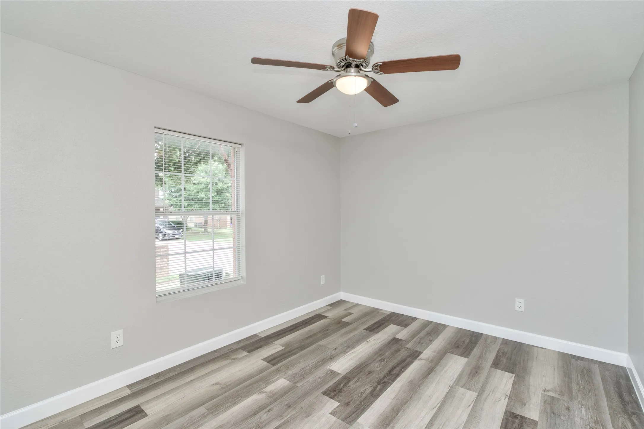Wood-finish flooring, ceiling fan with light fixture, window with blinds, and neutral wall tones