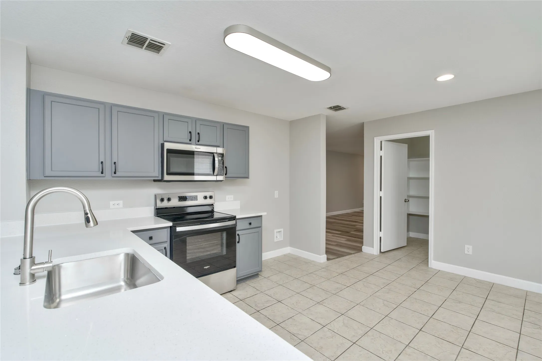 Kitchen featuring light gray cabinetry, stainless steel appliances, white countertops, and a stainless steel sink with a gooseneck faucet