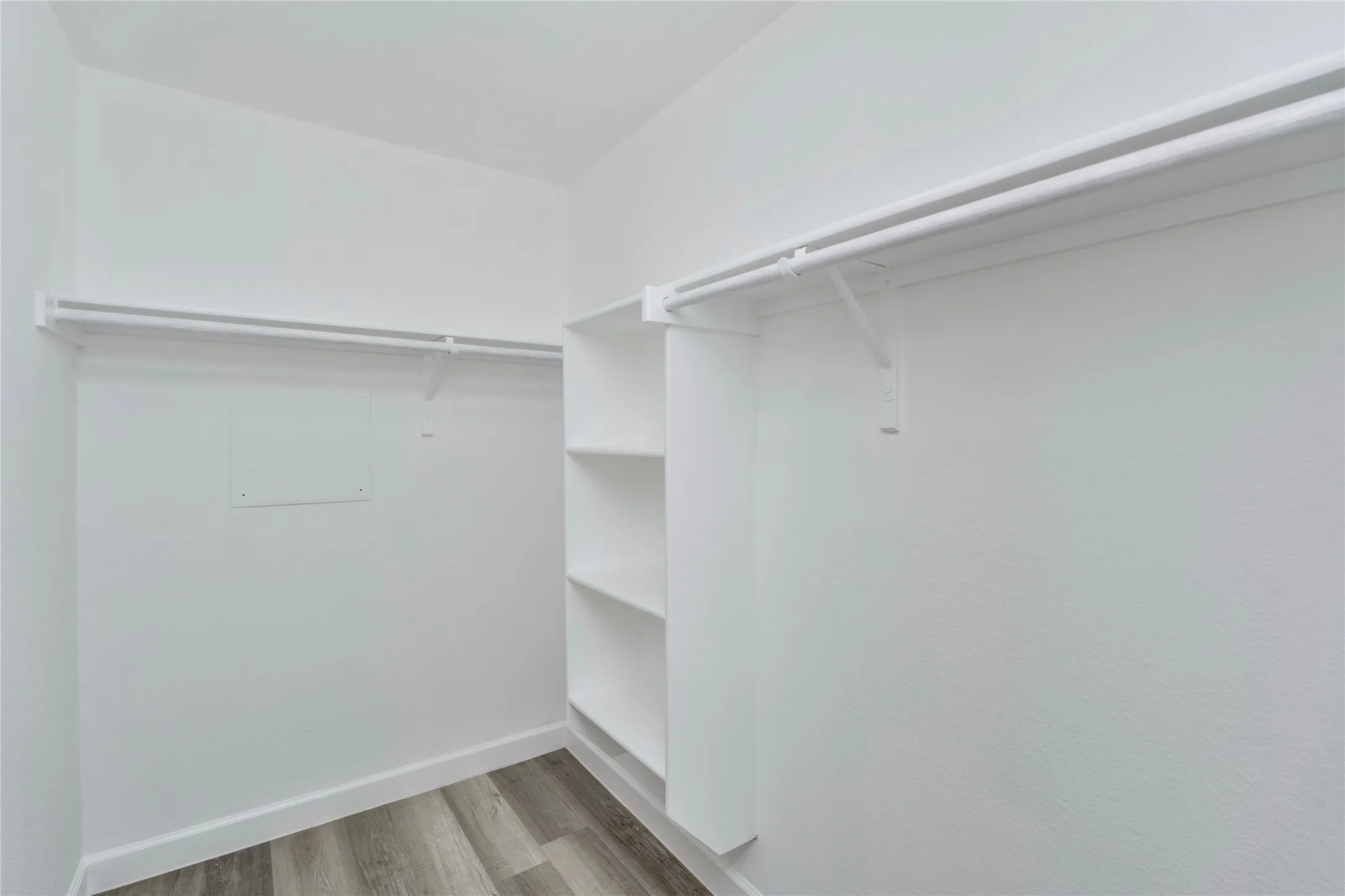 White walls, wood-finish flooring, built-in shelving, and dual clothing rods