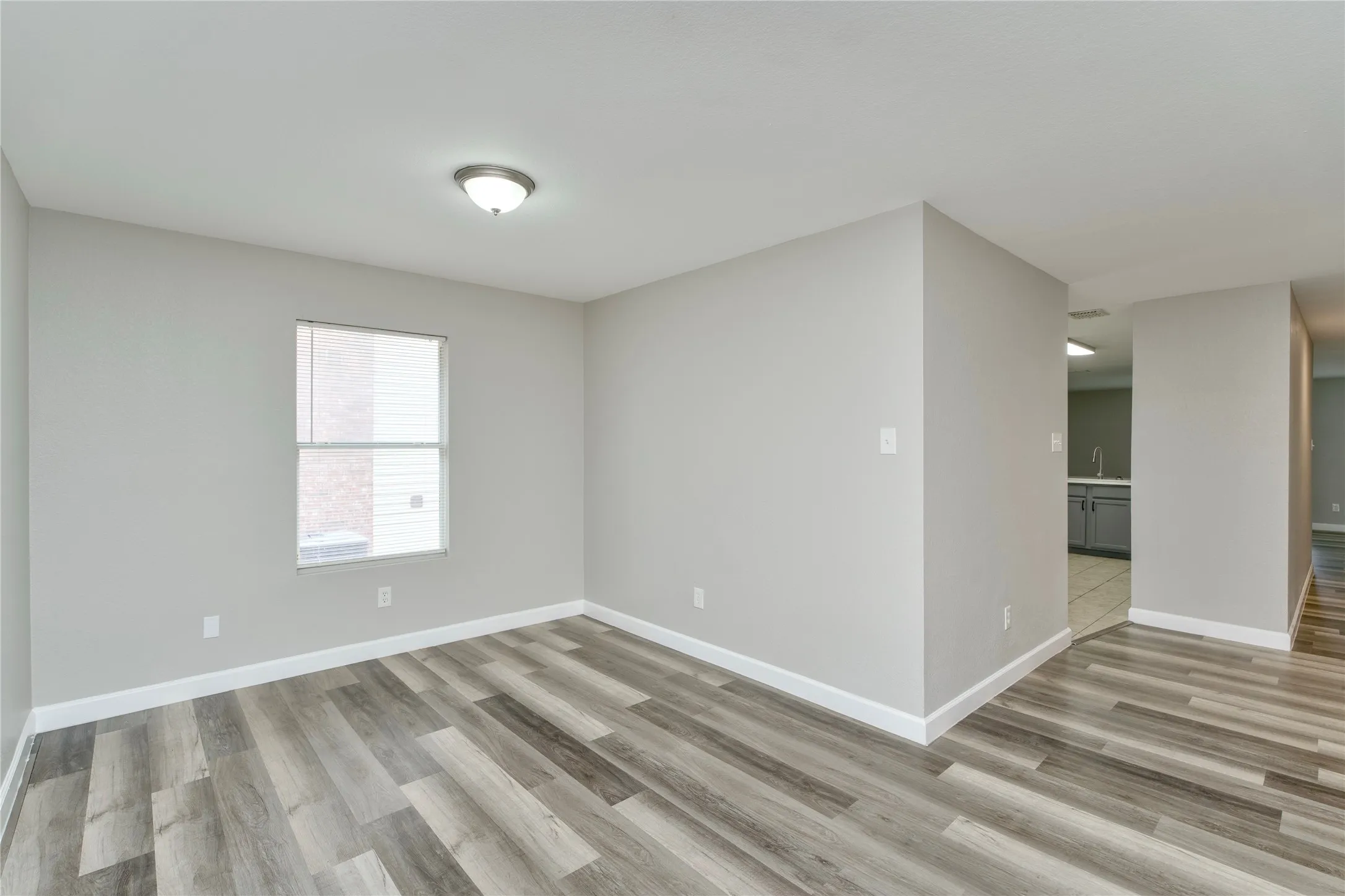 Contemporary interior with light gray walls, wood-finish flooring, a single window, and a flush-mount ceiling light