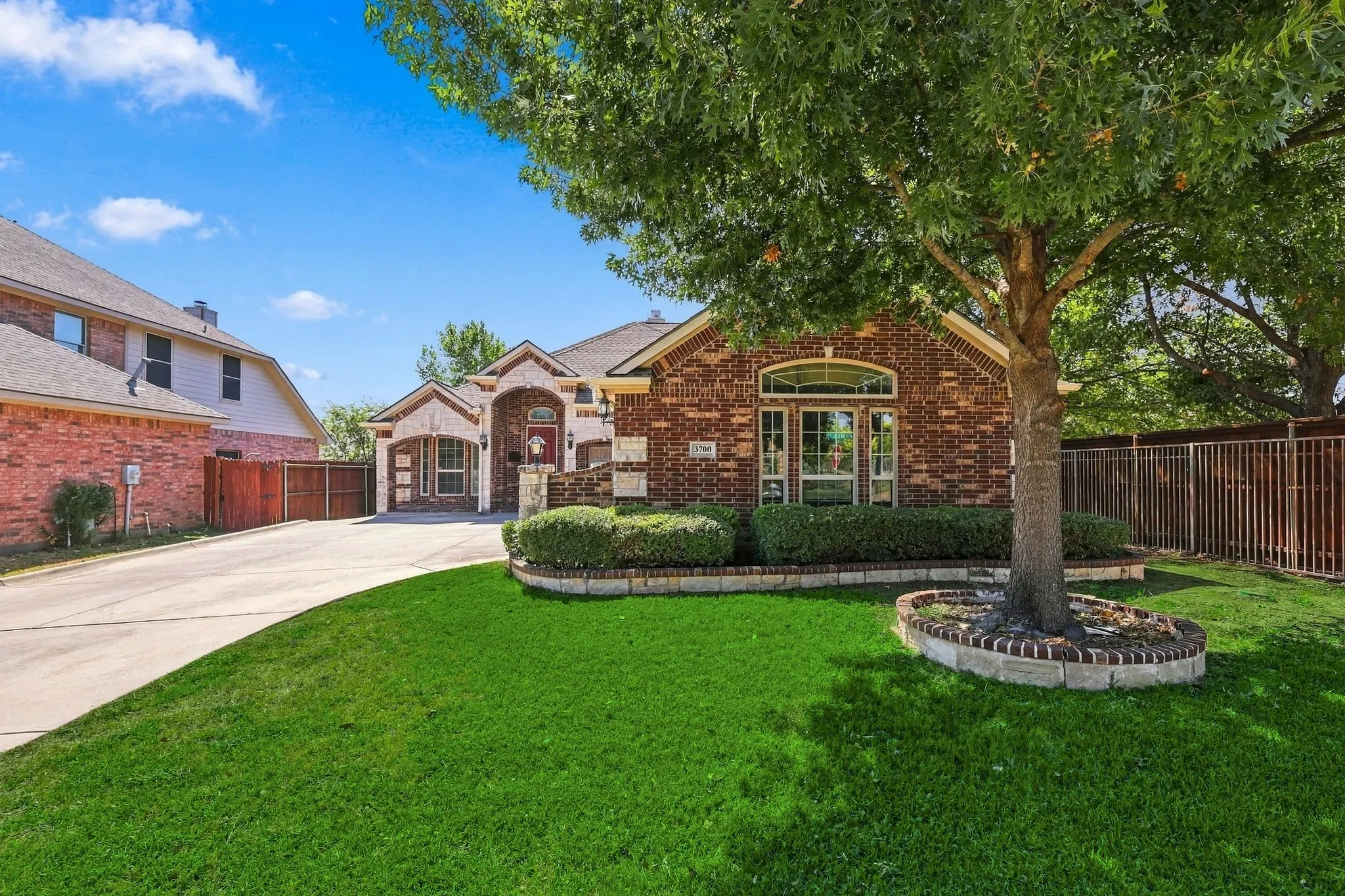 Brick exterior with stone accents, arched windows, manicured landscaping, mature trees, and a concrete driveway
