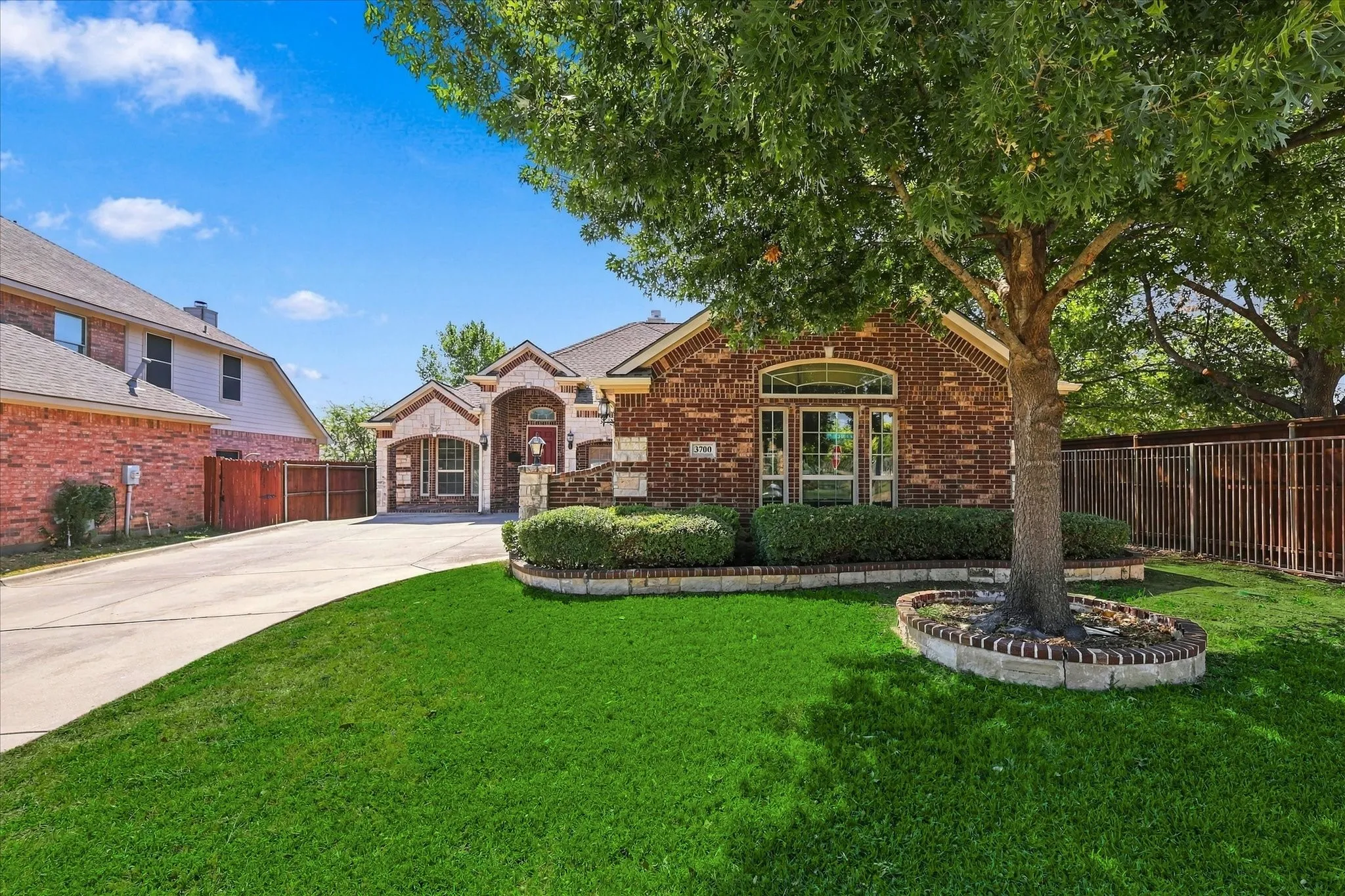 Brick facade, arched windows, covered entryway, mature tree, concrete driveway