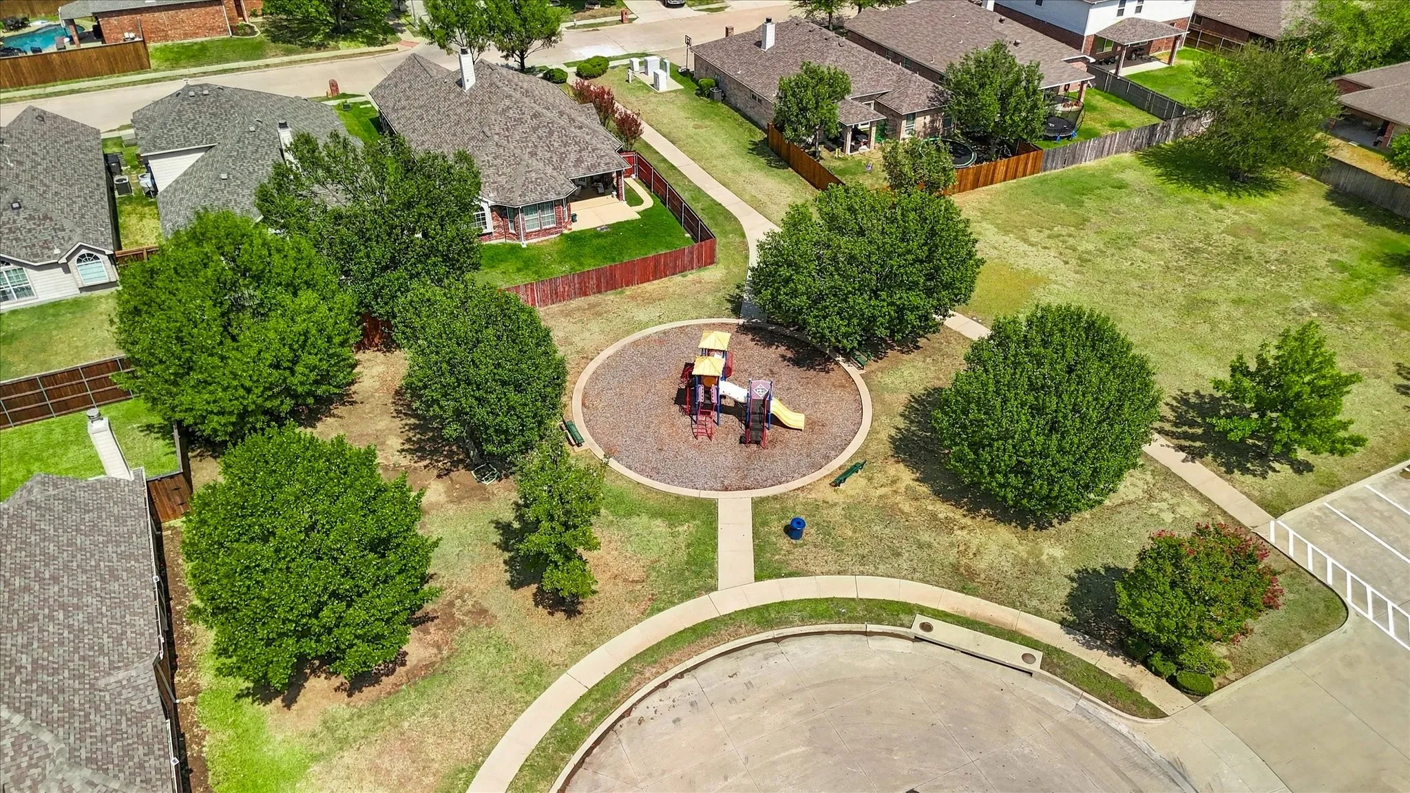 Centralized community playground with modern equipment, surrounded by landscaped green space, and bordered by concrete pathways