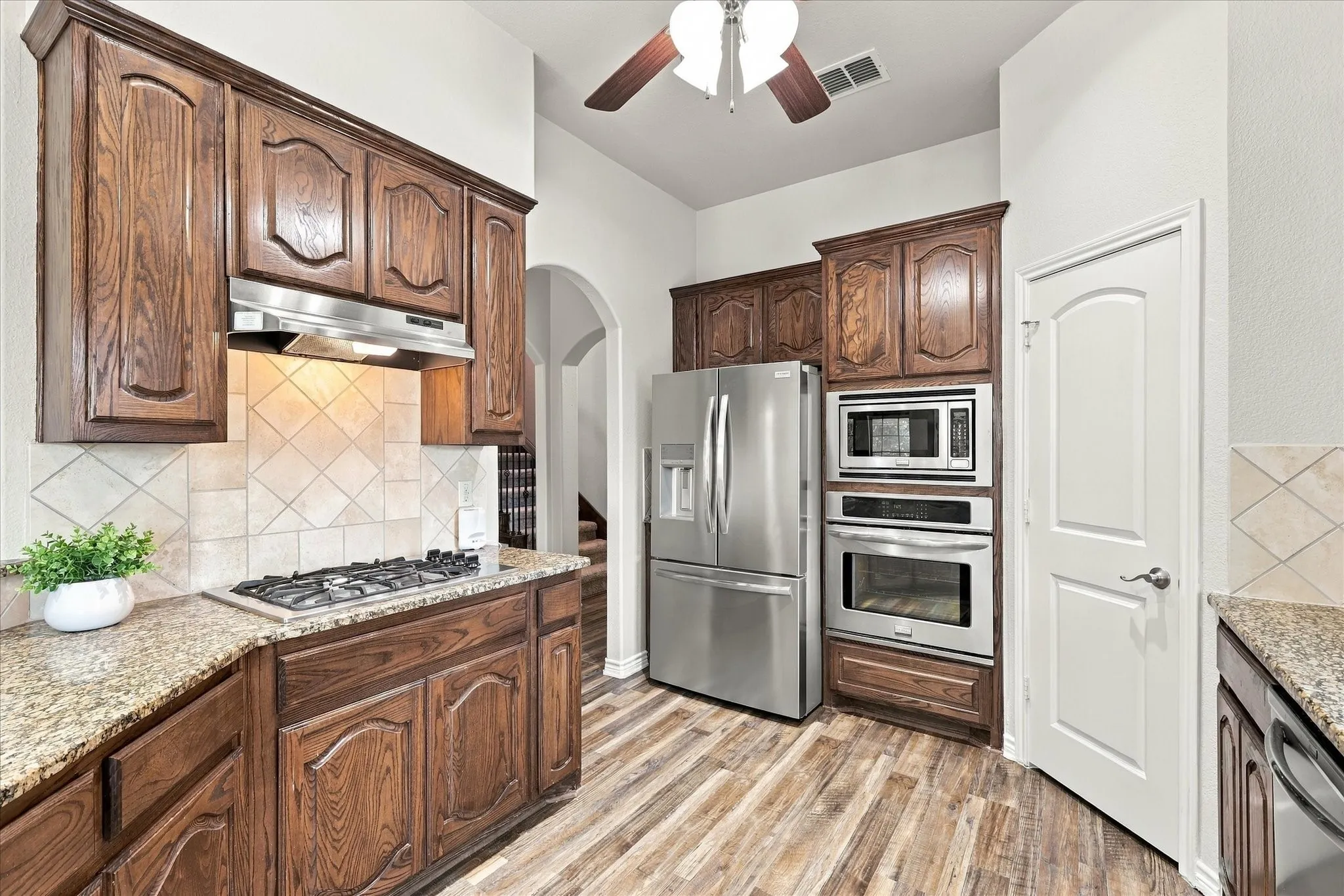 Wood-finish flooring, stainless steel appliances, built-in microwave, gas cooktop, and wood cabinetry