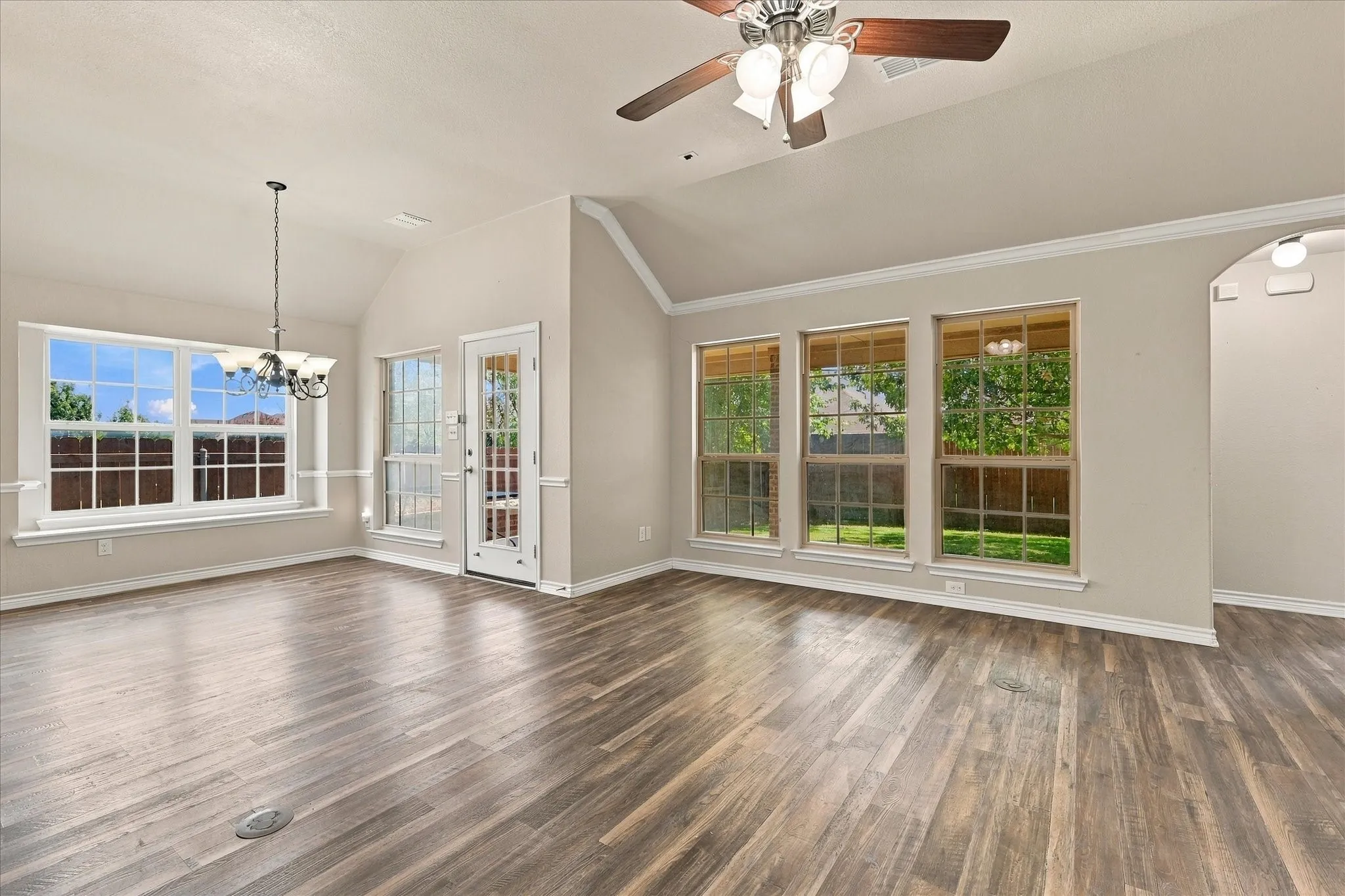 Vaulted ceiling, wood-finish flooring, multiple windows, ceiling fan, and chandelier lighting