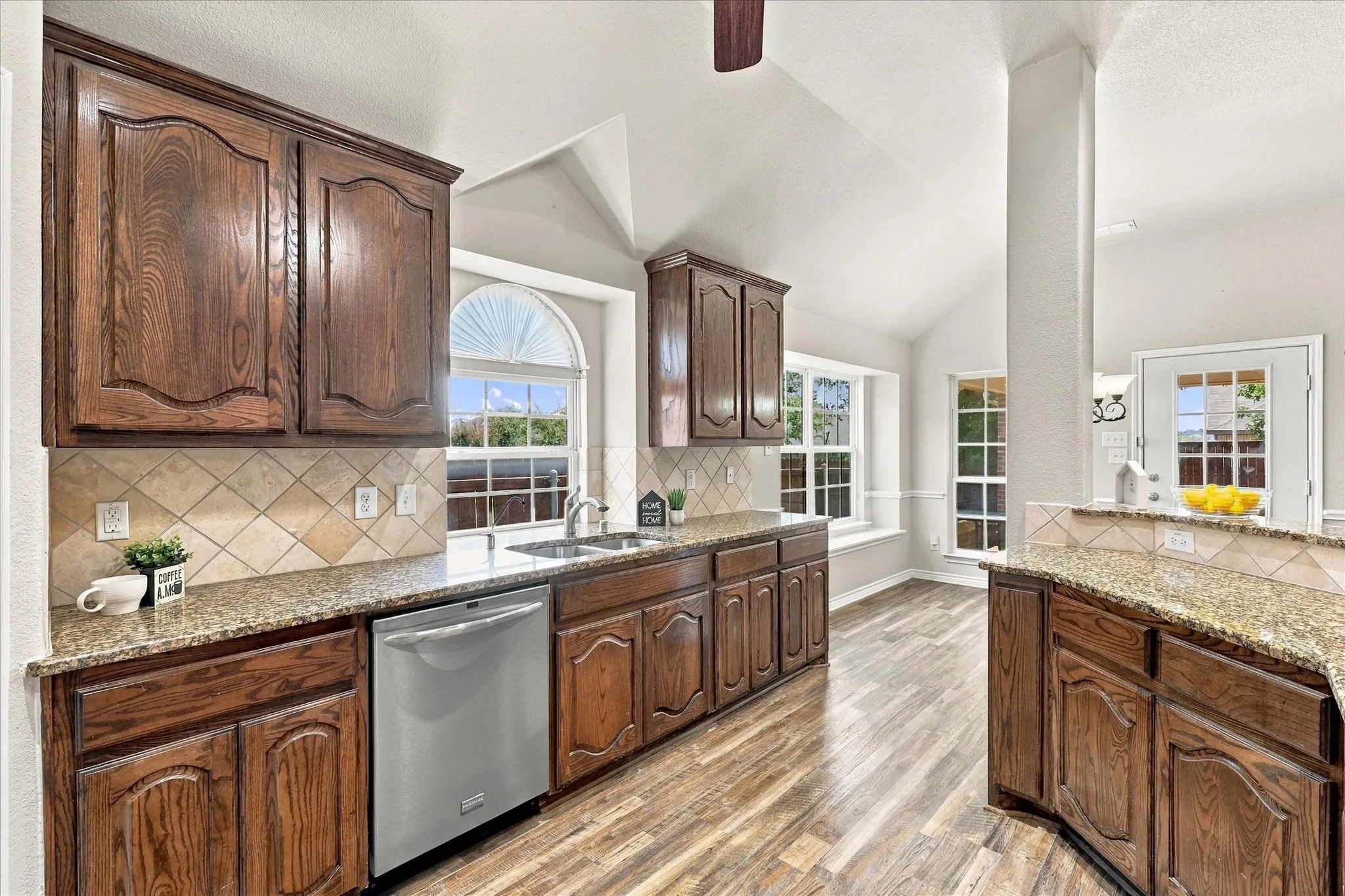 Kitchen featuring wood-finish flooring, vaulted ceilings, and granite countertops with a tile backsplash