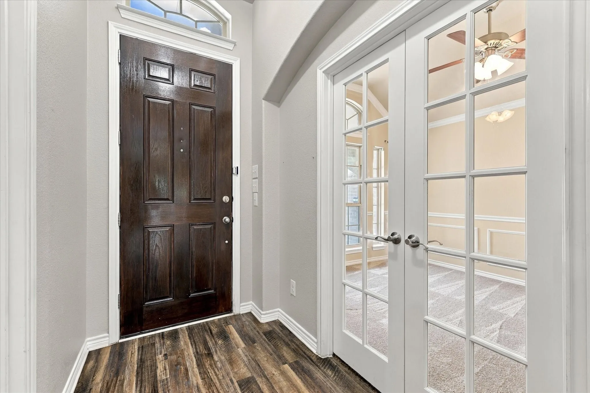 Rich wood-finish flooring, a paneled entry door with an arched transom, and white French doors with glass panes