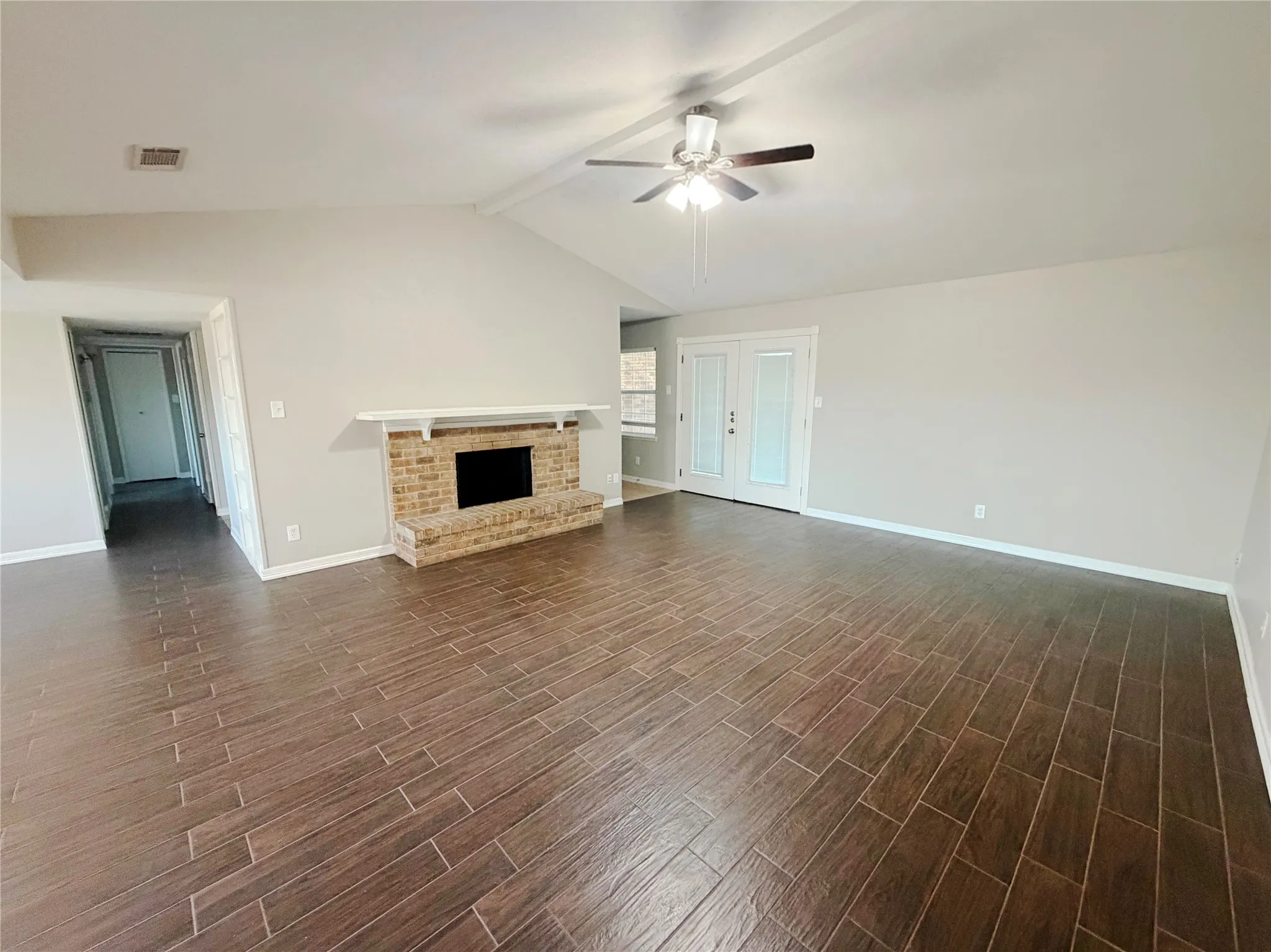 Spacious room featuring vaulted ceilings, wood-finish flooring, a brick fireplace, and double French doors