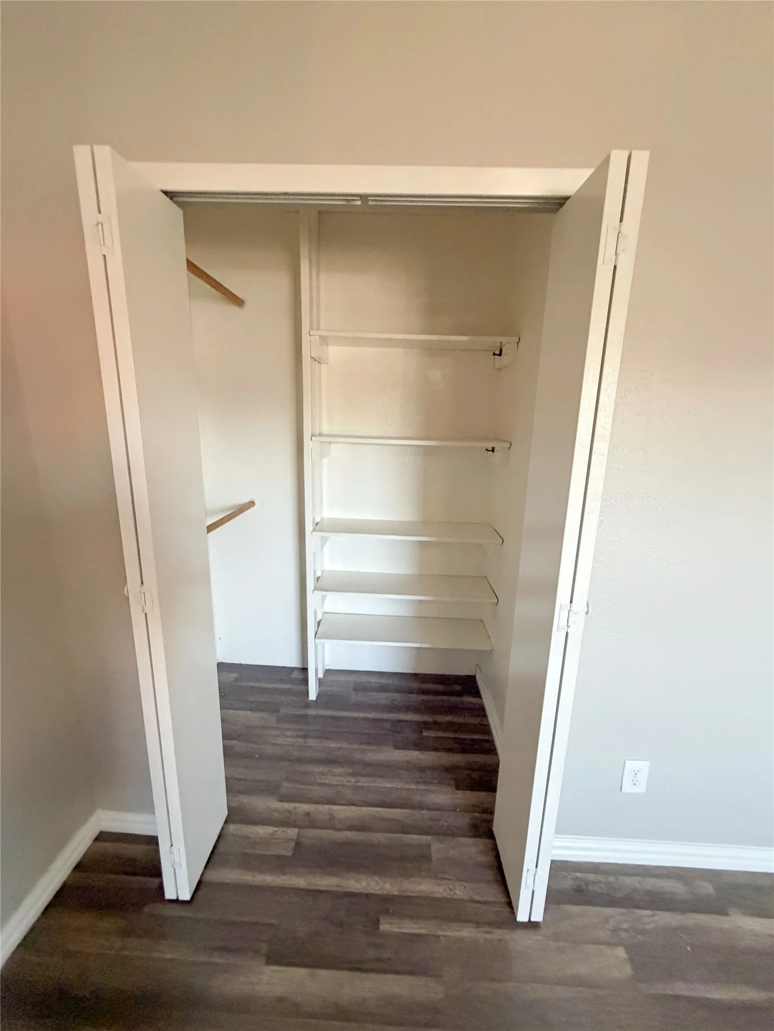 White bi-fold closet doors with interior shelving and clothing rods, set against wood-finish flooring
